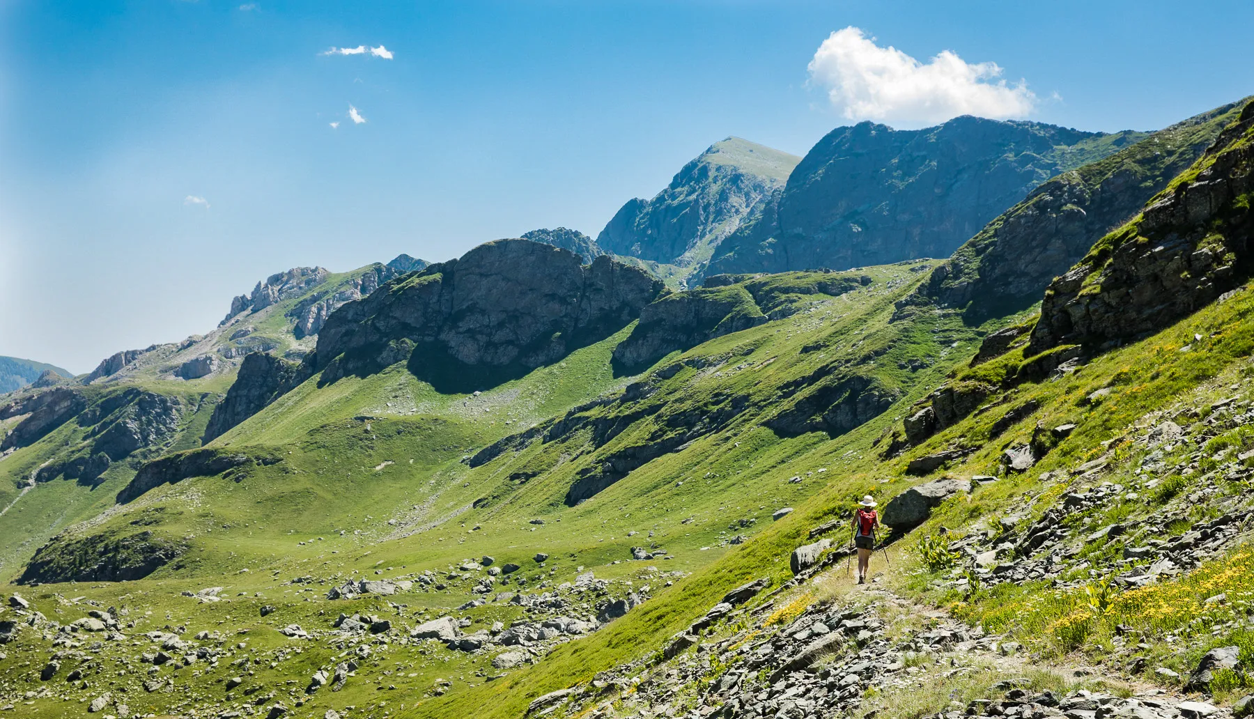 Solo hiker trekking a rocky slope along Kosovo’s Via Dinarica trail, surrounded by lush mountains.