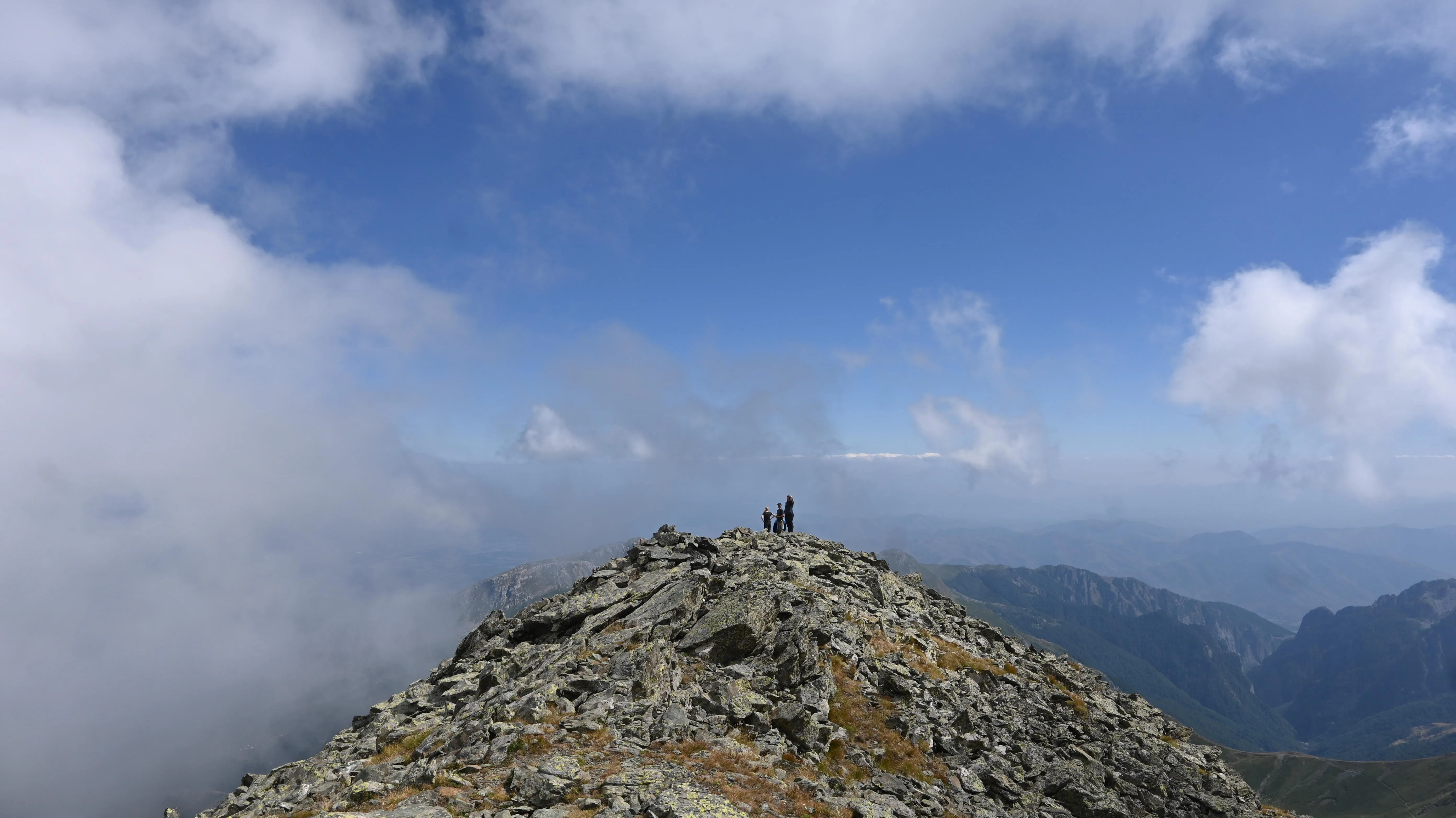 Hikers standing on a rocky peak with clouds around and vast mountain views along Kosovo’s Via Dinarica trail