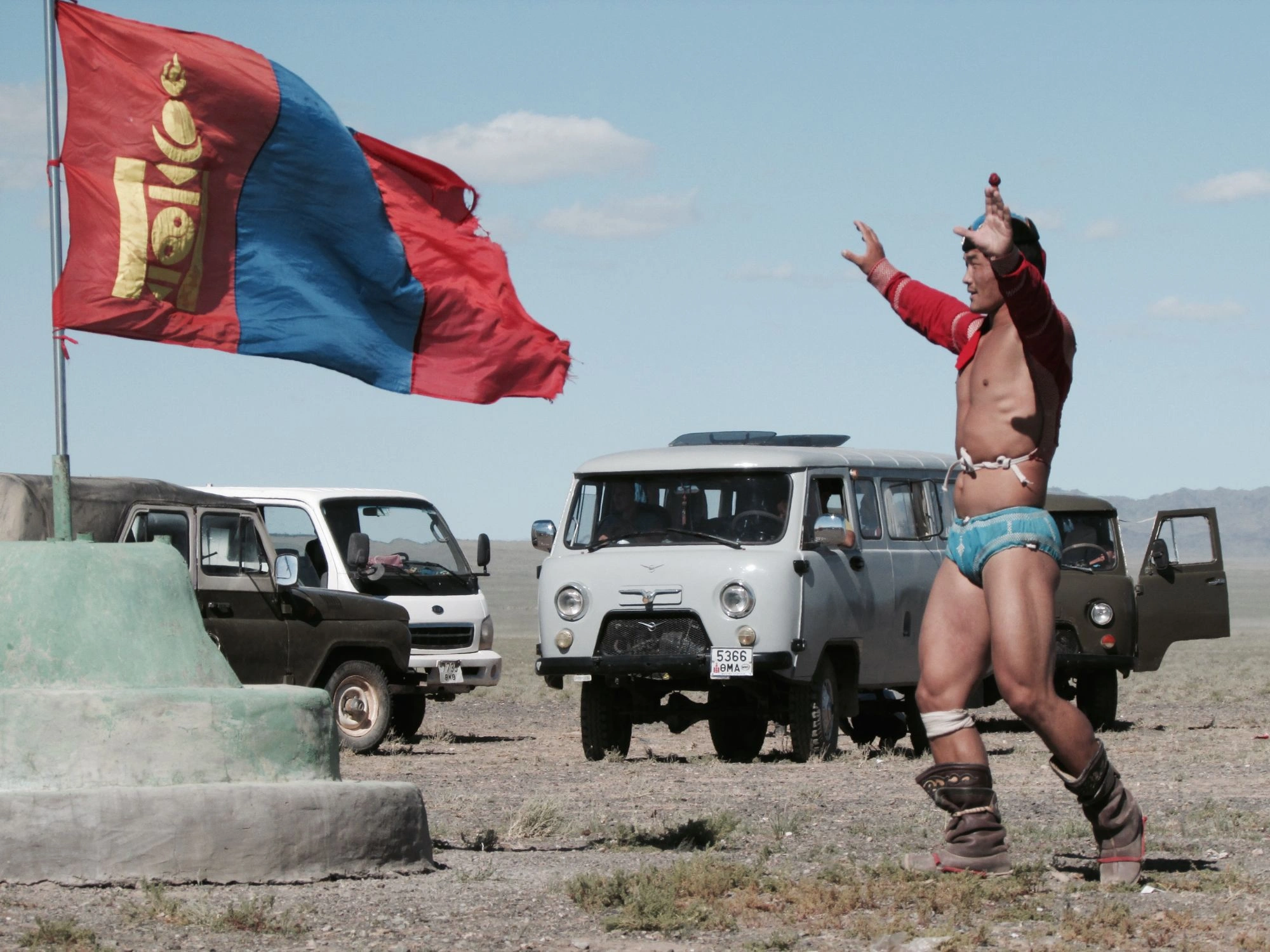 Mongolian wrestler celebrates at the Naadam festival with the Mongolian flag, blending culture and adventure travel.