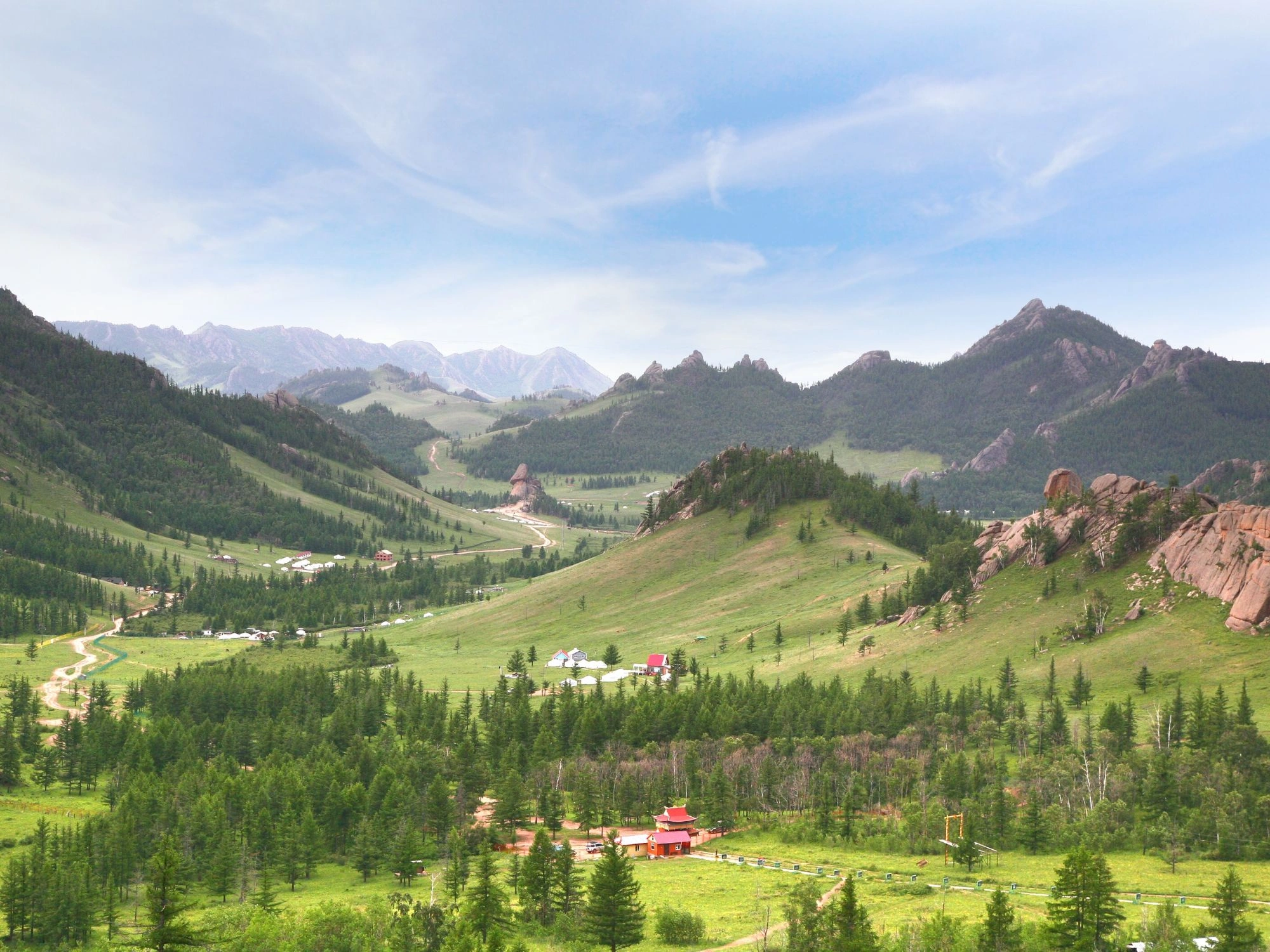 Rolling green hills, rocky cliffs, and scattered yurts in Terelj National Park, perfect for Mongolia trekking tours.