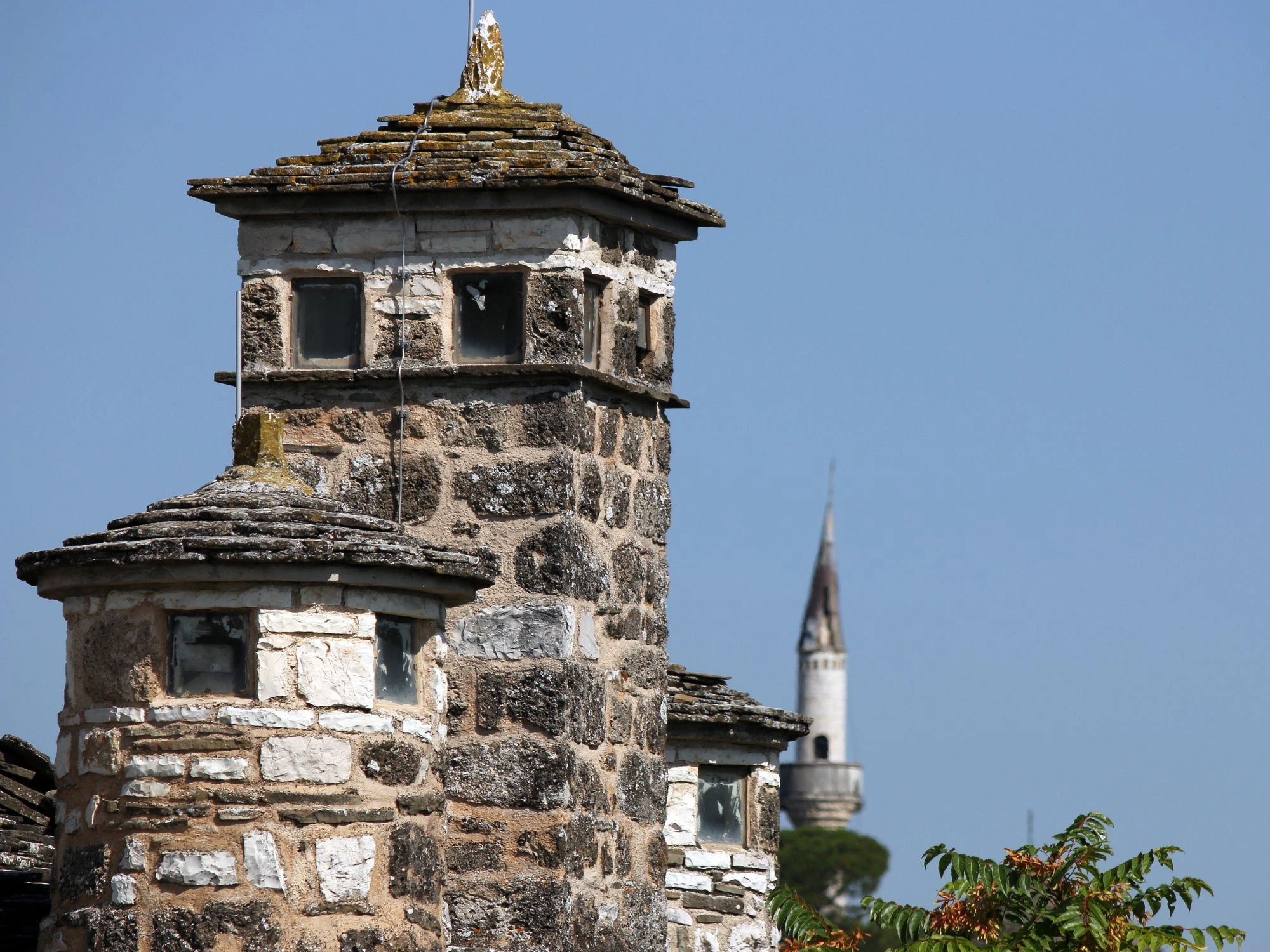 Traditional stone roof in Ioannina, Greece, with a distant view of a mosque minaret under clear blue skies.