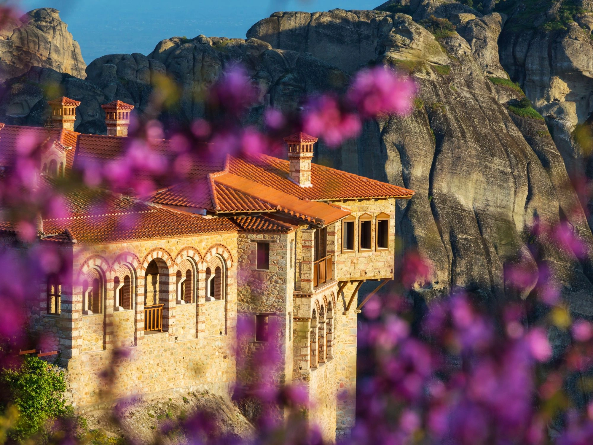 Greece Meteora monastery seen through purple flowers with rocky cliffs behind.