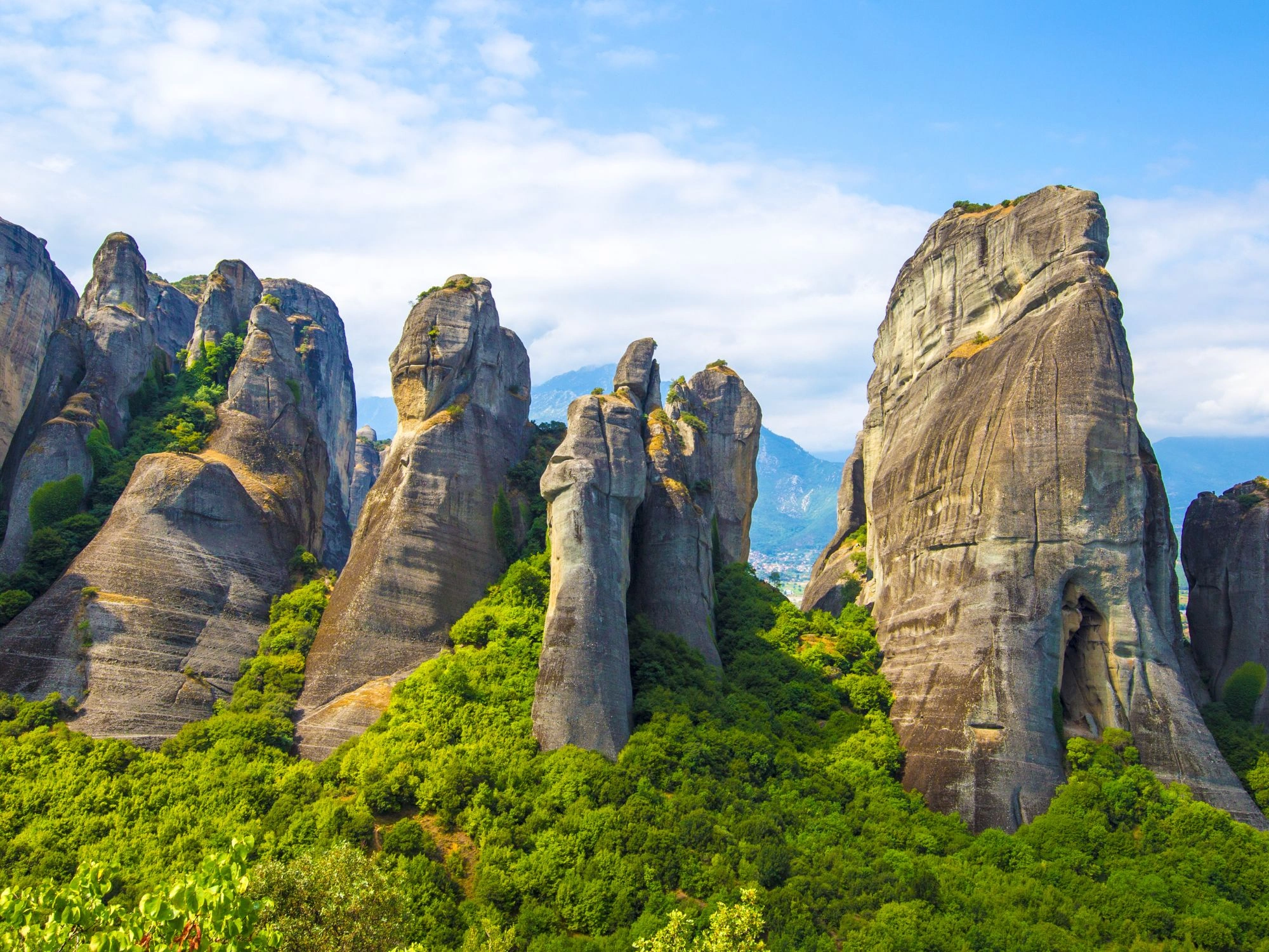 Towering rock formations in Meteora, Greece, with green forest nestled between the dramatic stone pillars.