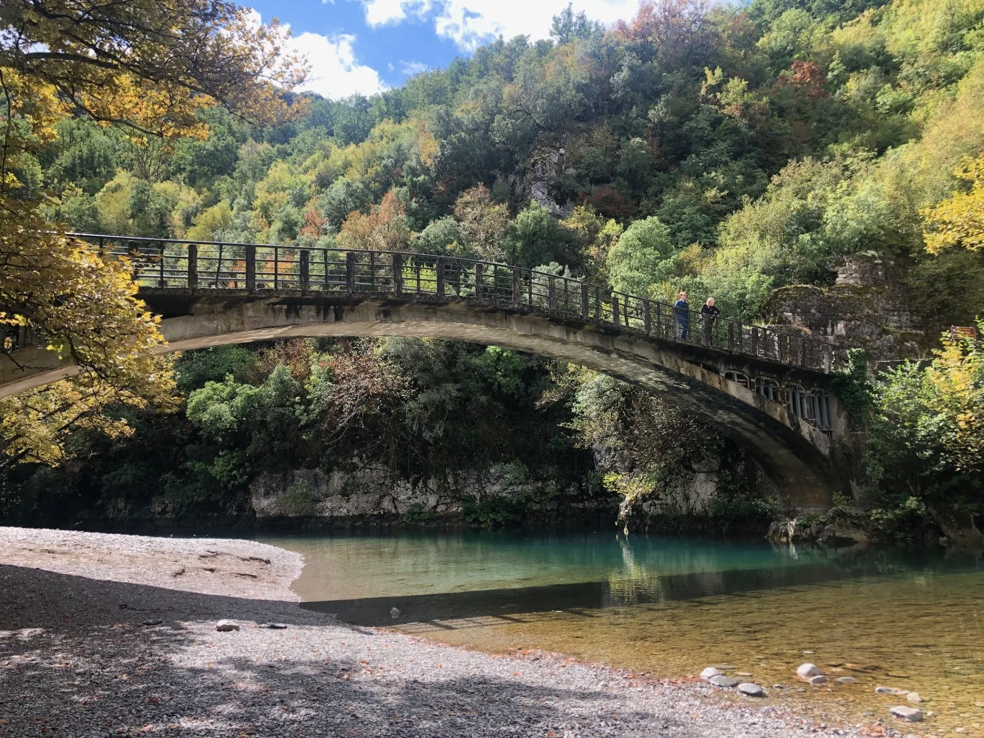 Stone bridge over Voidomatis River, reflecting autumn trees, in the heart of Zagori, Epirus, Greece.