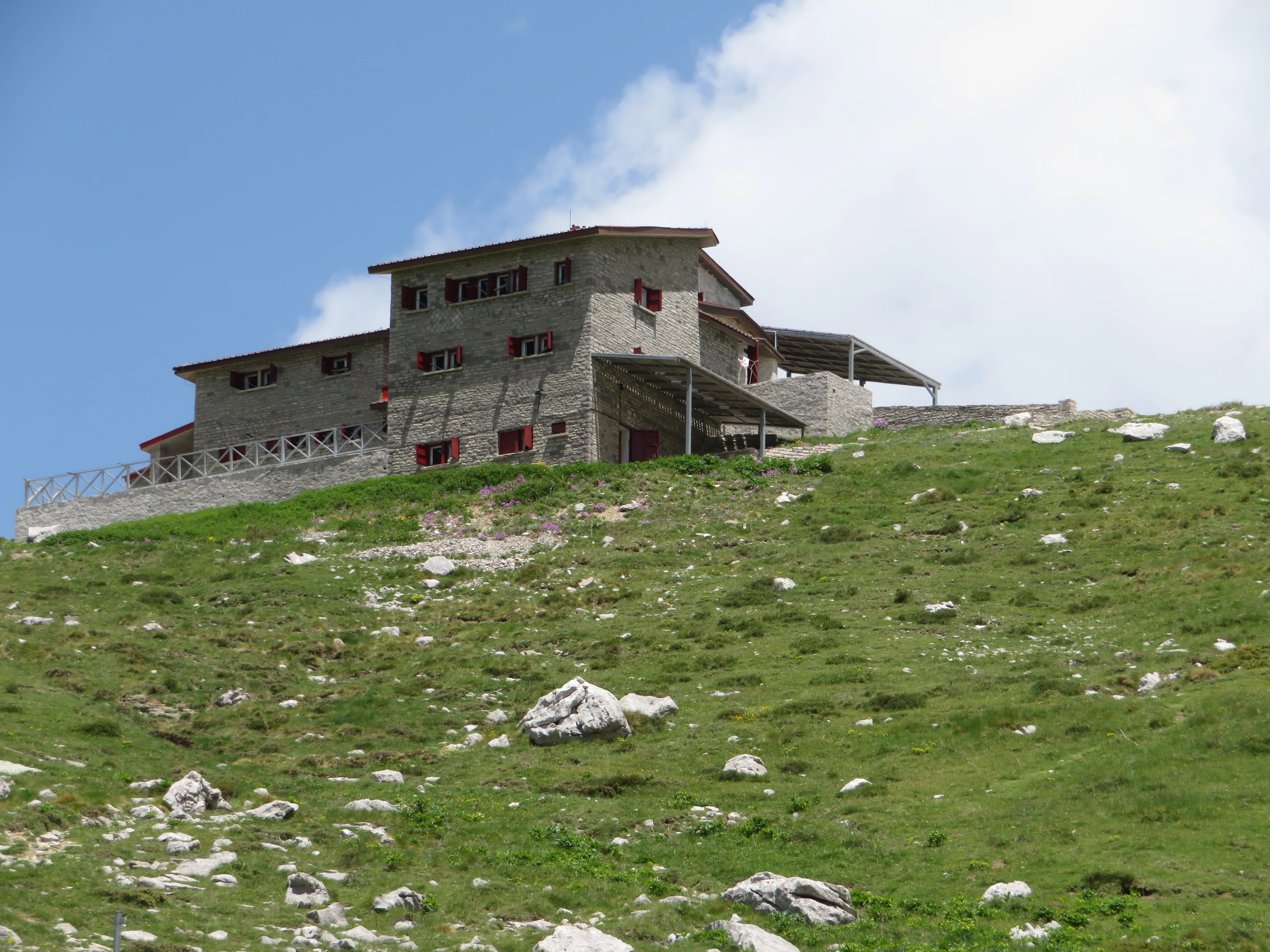 Stone mountain refuge with red shutters on a grassy hilltop in the Astraka region of Epirus, Greece.