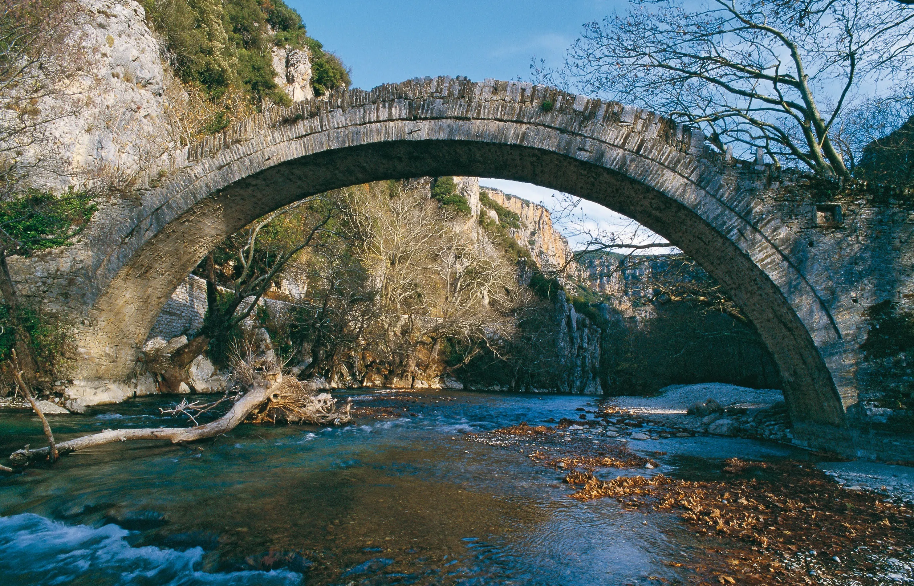 Stone arch bridge crossing the clear waters of Voidomatis River near Kleidonia, Epirus, Greece.