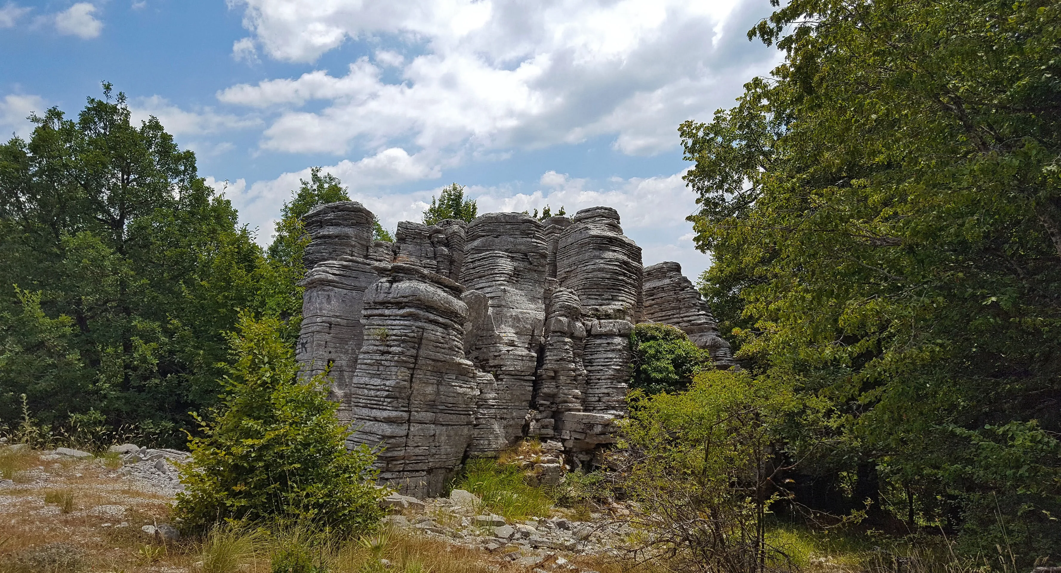 Unique stone formations stacked like towers, surrounded by lush green trees in Epirus, Greece.