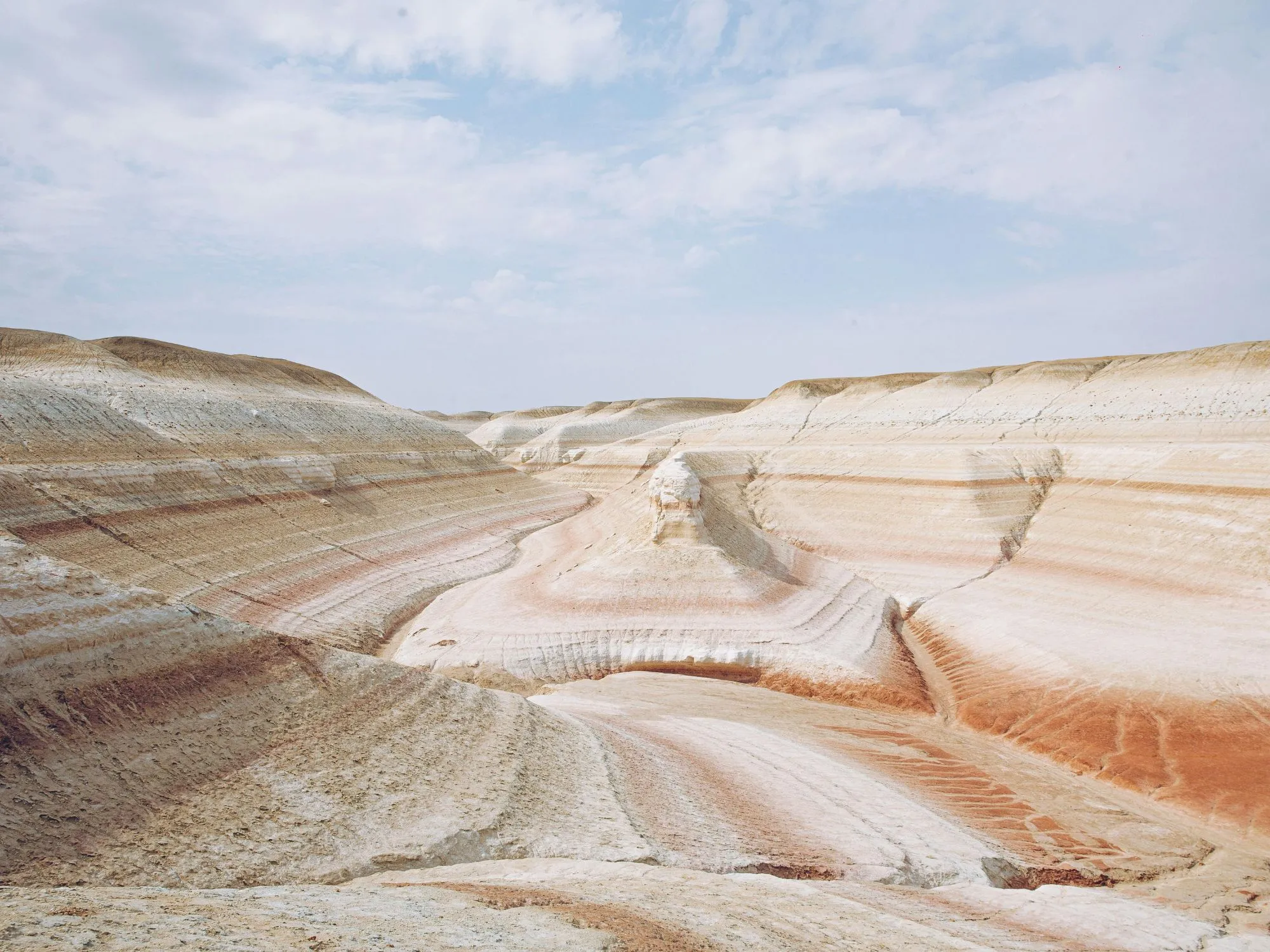 The Kyzylkup area in Kazakhstan, featuring undulating sandstone formations in shades of red and beige, shaped by wind and time.
