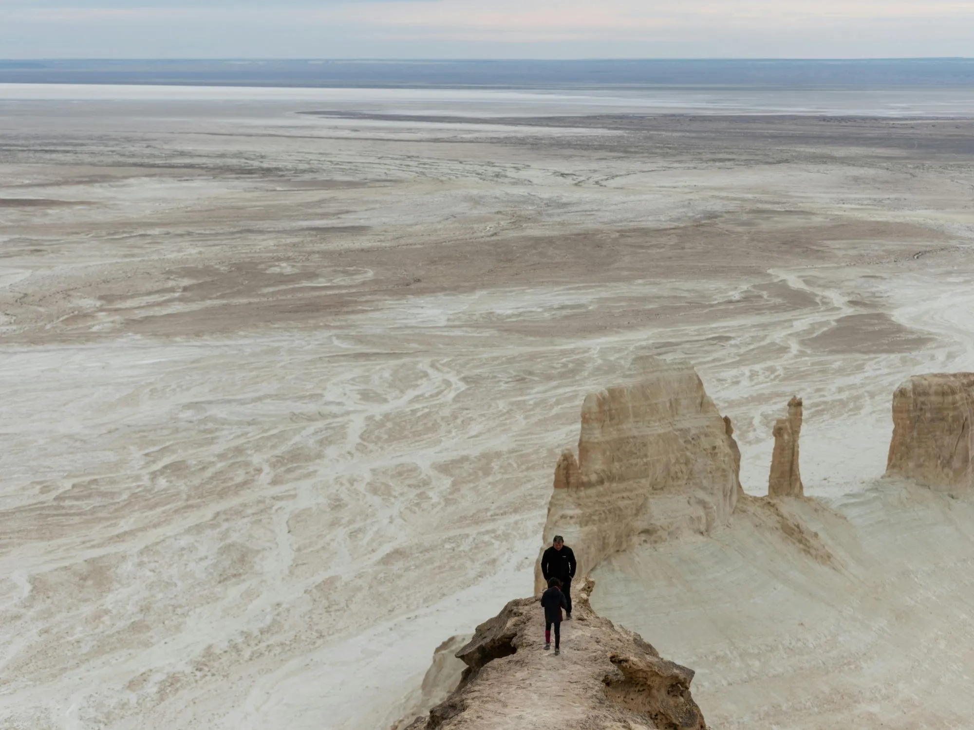 A group of hikers exploring the dramatic Bozzhyra rock formations in Kazakhstan’s Mangystau region, surrounded by towering white cliffs and deep valleys.