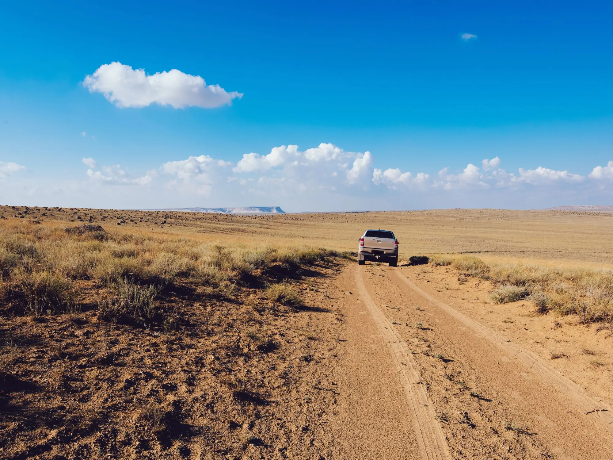 A lone off-road vehicle drives along a dusty trail through Mangystau’s vast open plains under a brilliant blue sky.