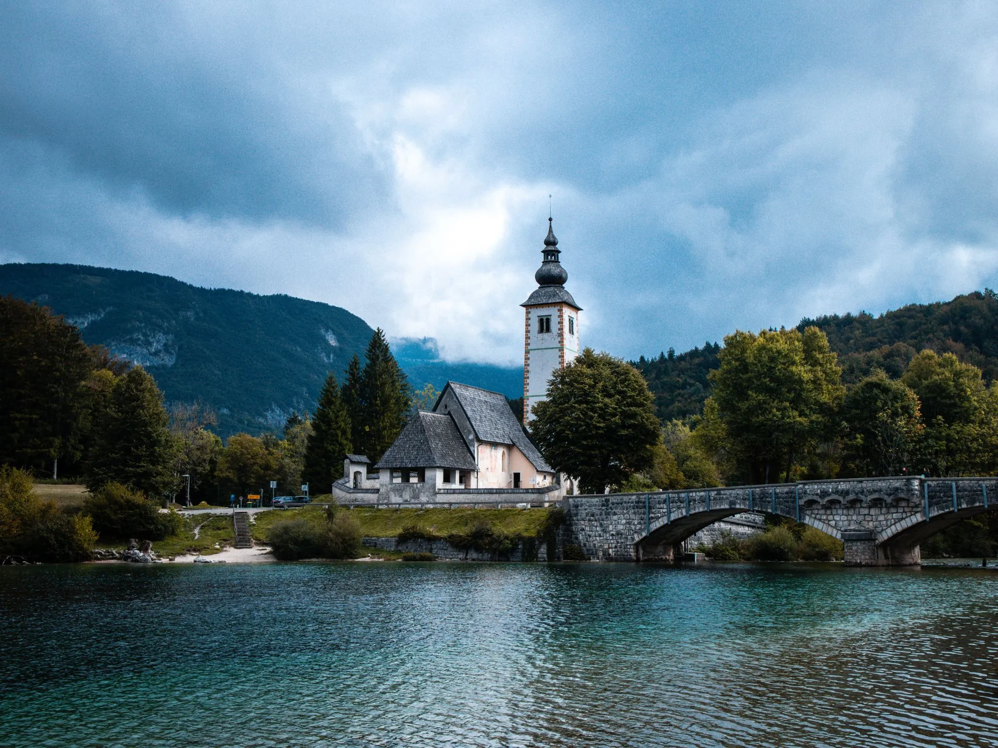 Historic Church of St. John the Baptist overlooking Lake Bohinj, Slovenia, framed by emerald waters and lush mountain scenery – cultural gem of the Julian Alps.