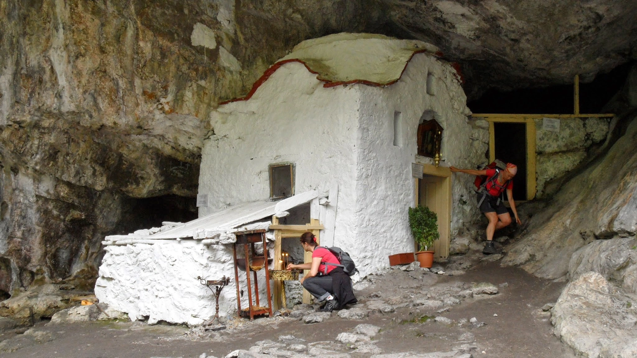 Remote cave chapel hidden within Mount Olympus, Greece, with hikers stopping to explore and light candles inside.