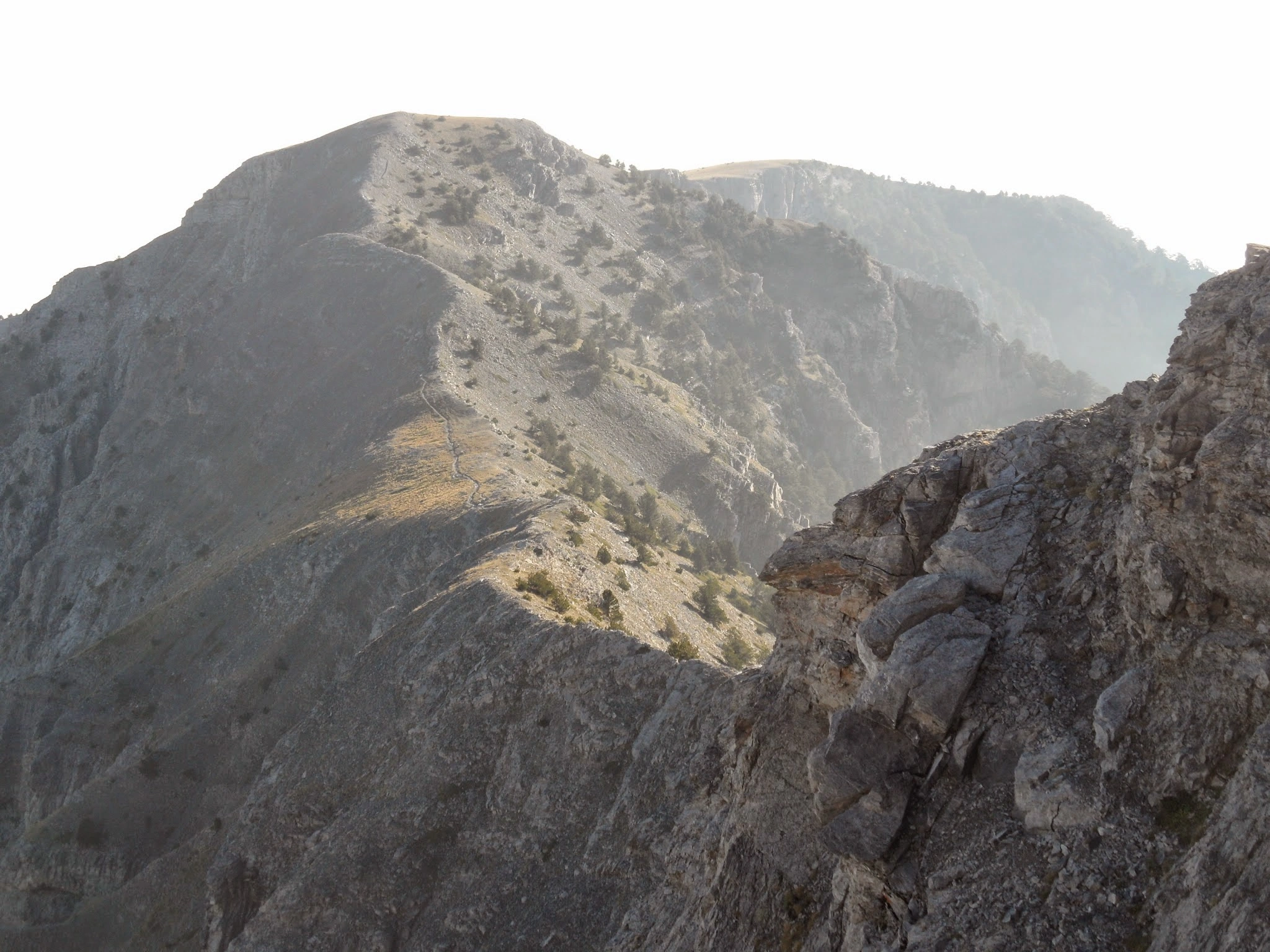 Narrow ridgeline hiking trail along Mount Olympus, Greece, surrounded by rocky slopes and panoramic mountain views.