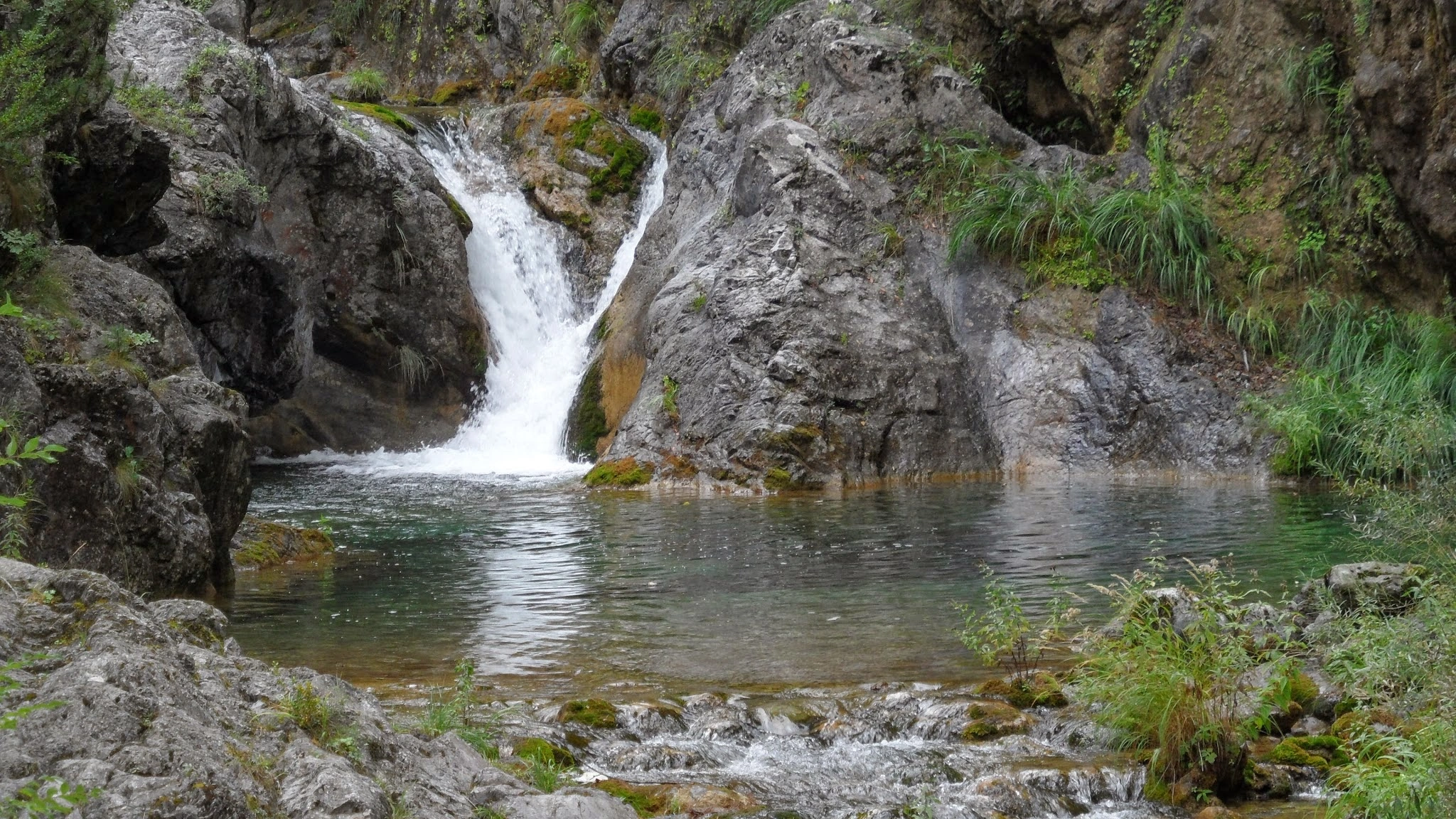 Small waterfall cascading into a turquoise pool, surrounded by mossy rocks in Enippeus Gorge, Mount Olympus, Greece.