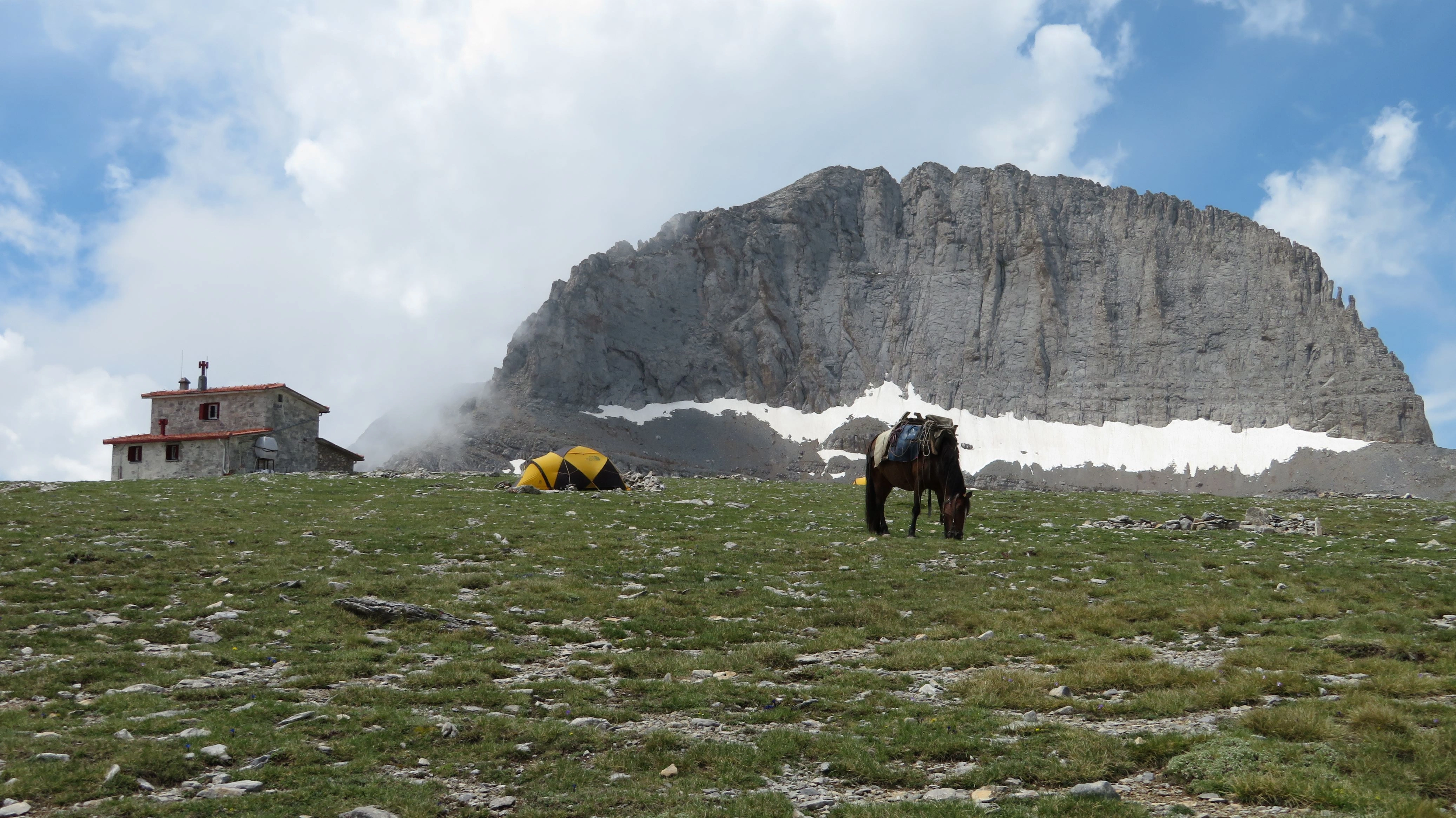View of Stefani Peak, the Throne of Zeus, with Kakalos Mountain Hut and yellow tents on Mount Olympus, Greece.