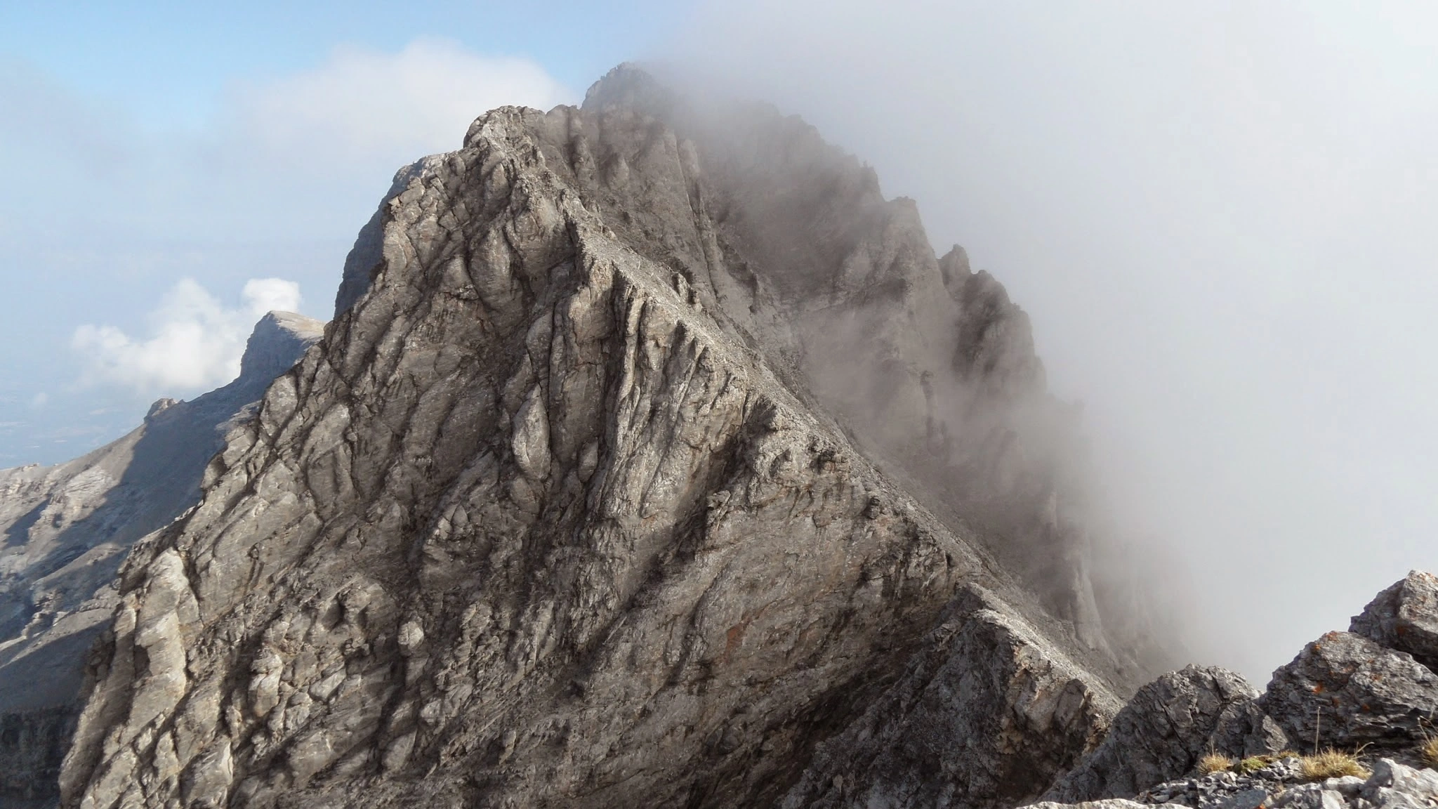 Dramatic mist-covered rocky ridge along a hiking trail on Mount Olympus, Greece, showcasing the rugged alpine terrain.