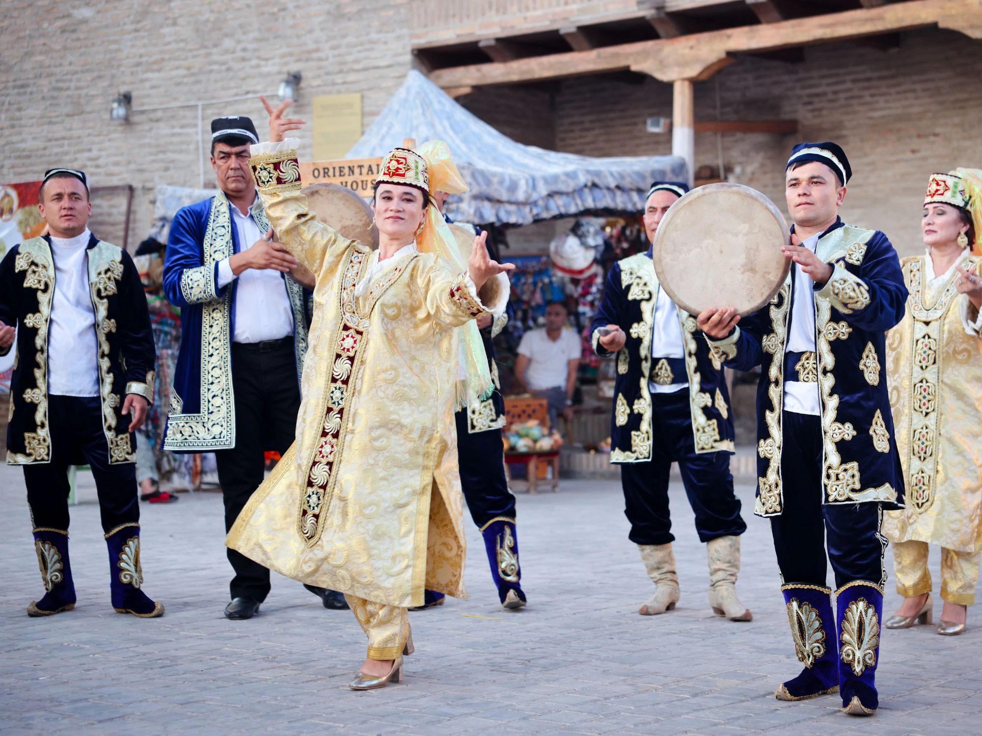Traditional Uzbek dancers in colorful embroidered costumes performing a lively cultural dance at an outdoor heritage festival in Uzbekistan.