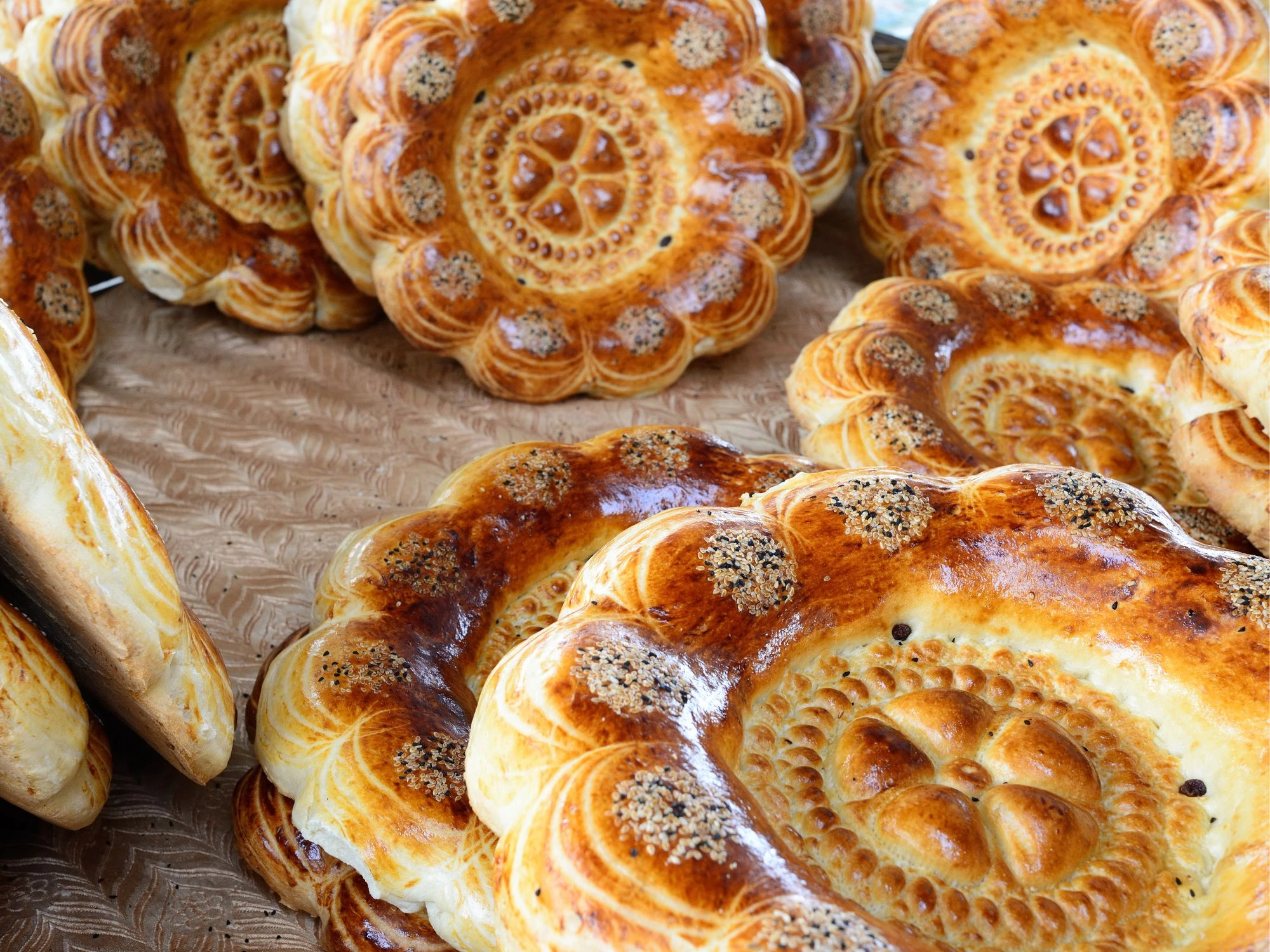 Traditional Uzbek bread with intricate circular patterns, golden crust, and sesame seeds, displayed at a local market in Uzbekistan.