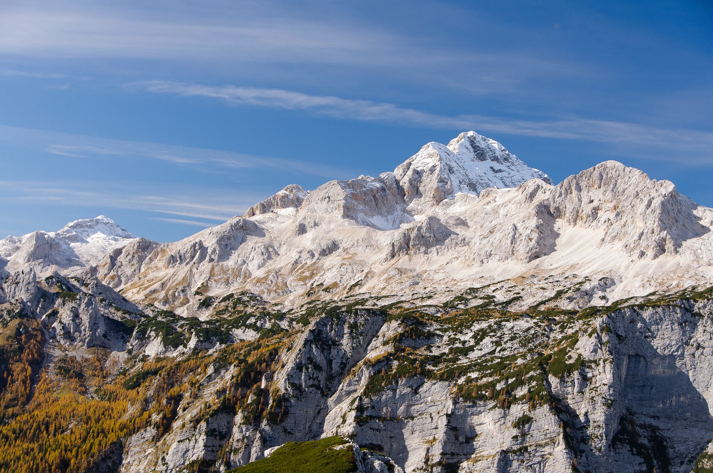 Majestic snow-capped peak of Mount Triglav in the Julian Alps, Slovenia, with autumn trees in the foreground – top trekking destination.