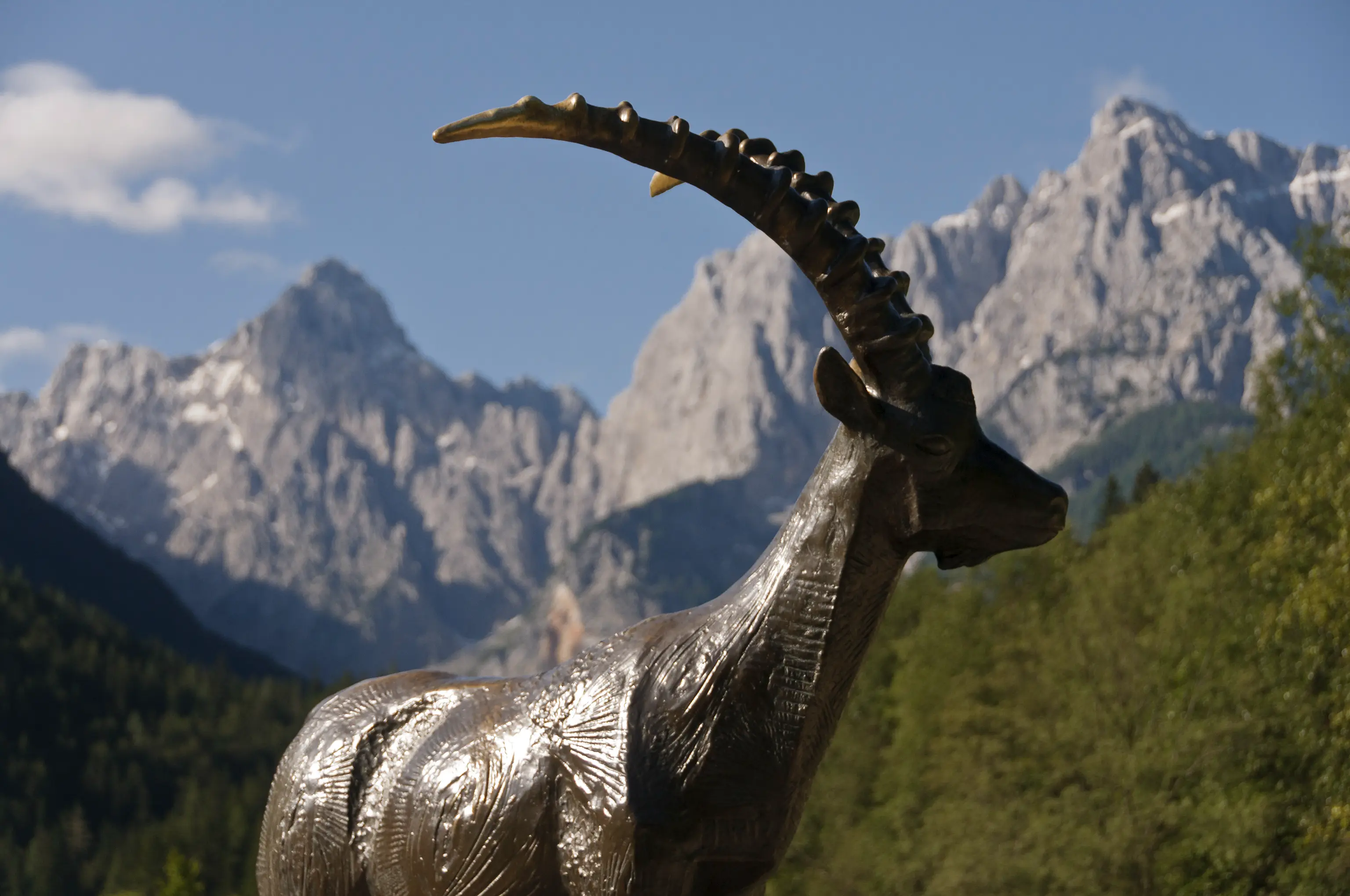 Close-up of ibex statue with Slovenian Alps peaks behind, a scenic stop for hikers and walkers.