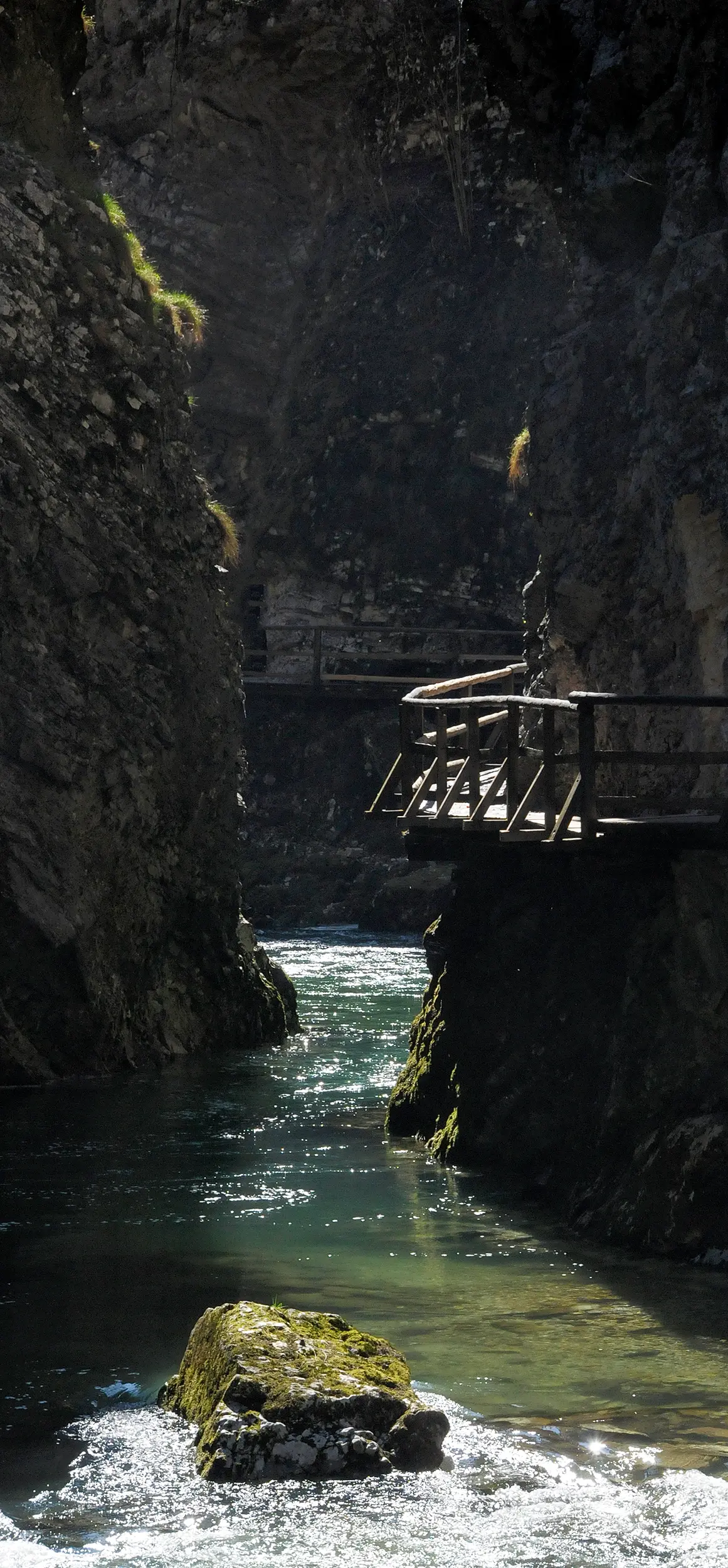 Close-up view of a narrow river canyon with a wooden footbridge hanging over the shimmering water below.