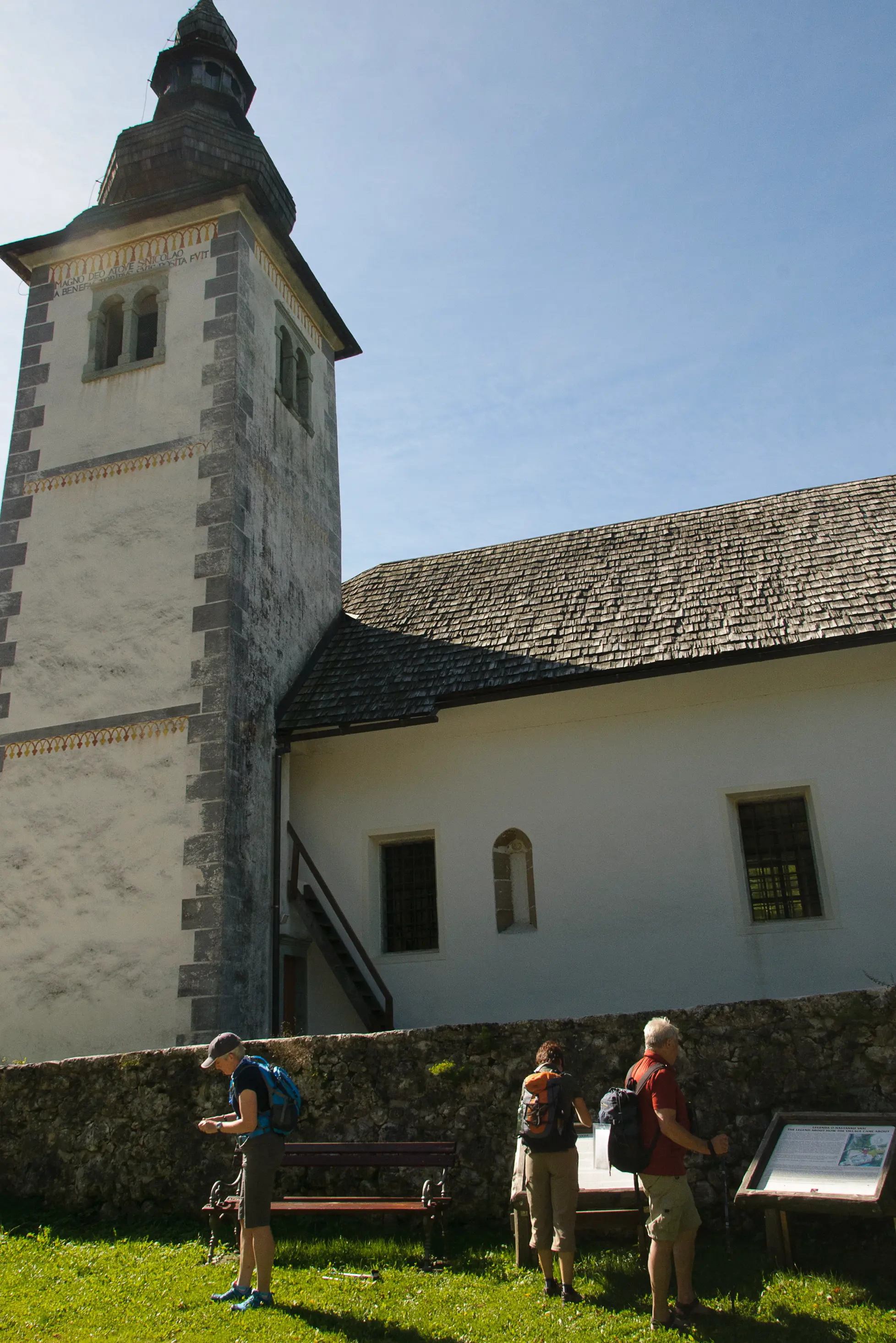 Historic stone church with a tall bell tower, hikers exploring the grounds and reading information signs.