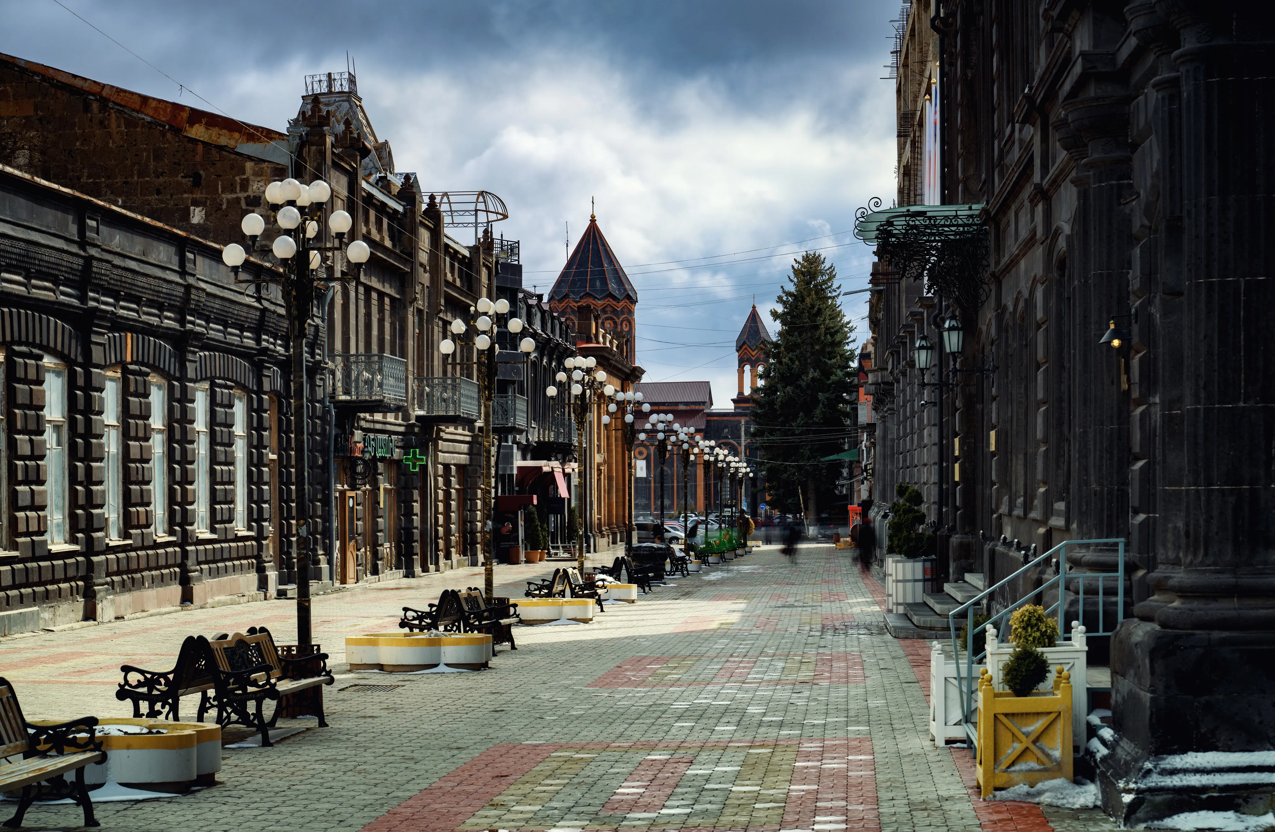 Historic street in Gyumri, Armenia, featuring black stone buildings, European-style street lamps, and a cloudy sky.