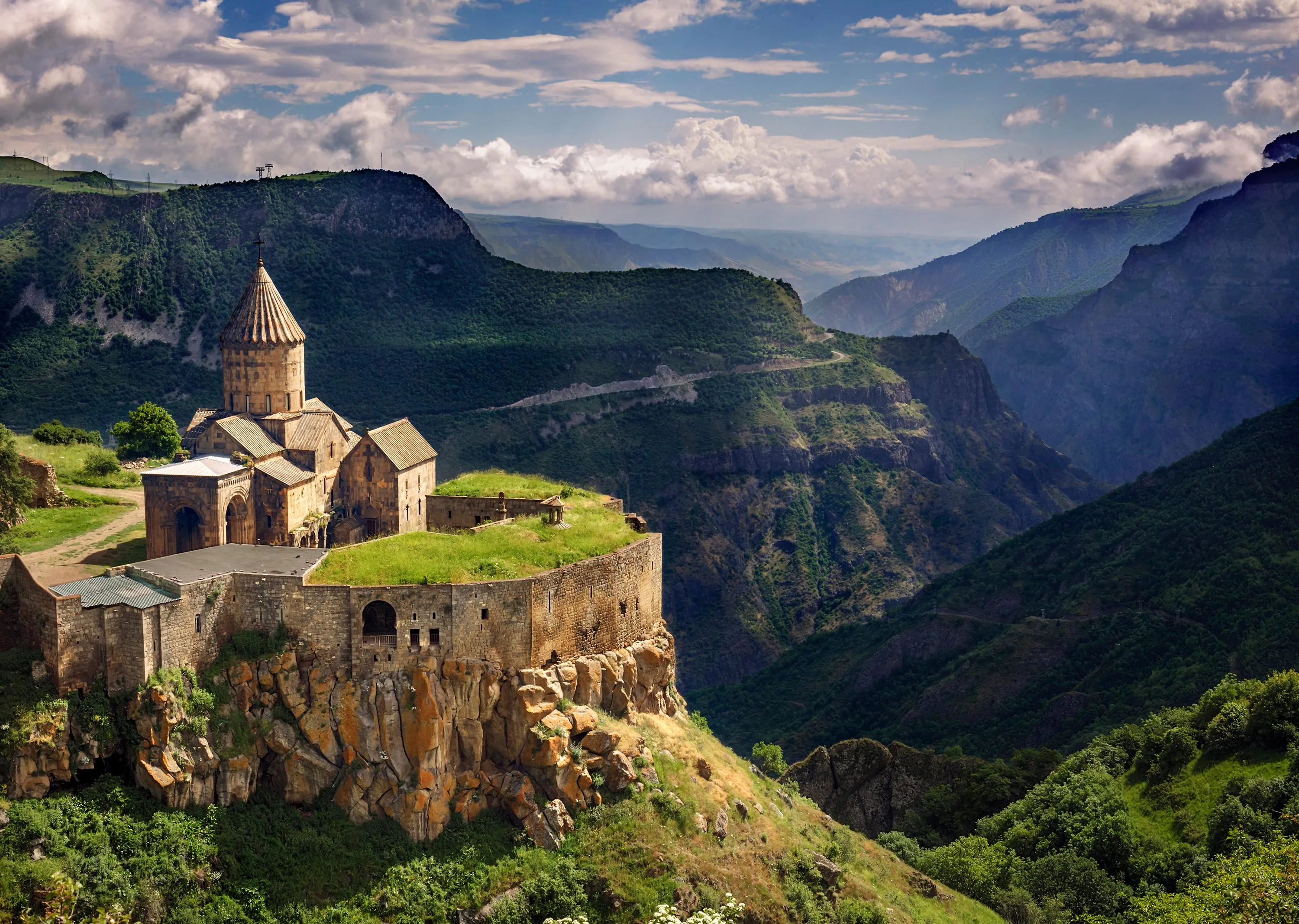 Tatev Monastery on a cliffside in Armenia, surrounded by lush green mountains and deep gorges.