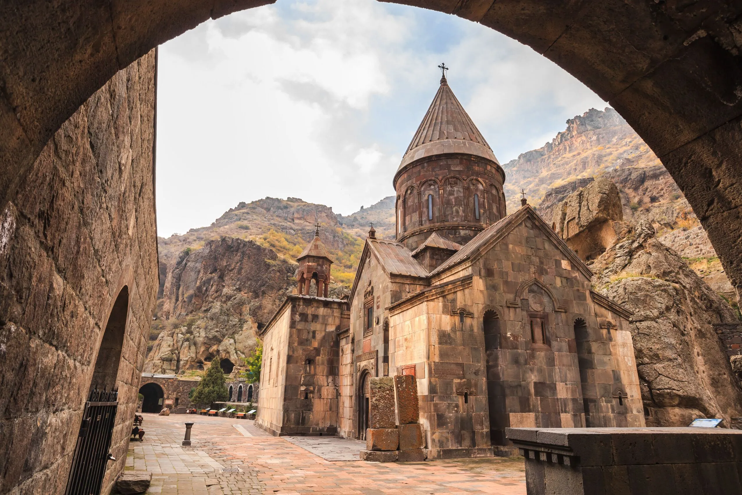 Geghard Monastery in Armenia, a medieval rock-cut church framed by an ancient stone archway and mountain cliffs.