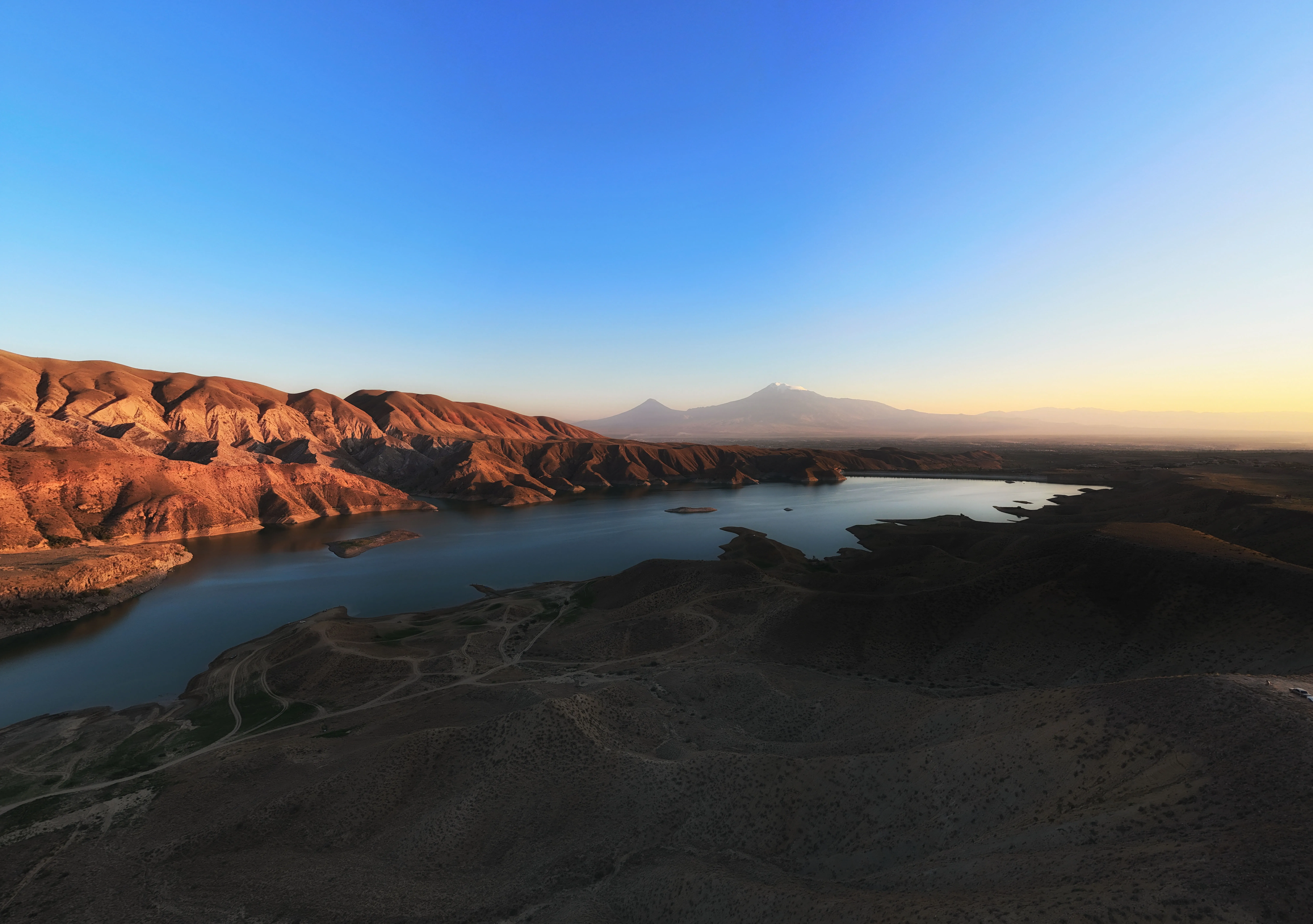The Azat Reservoir in Armenia, surrounded by rugged hills with Mount Ararat visible in the distance at sunset.