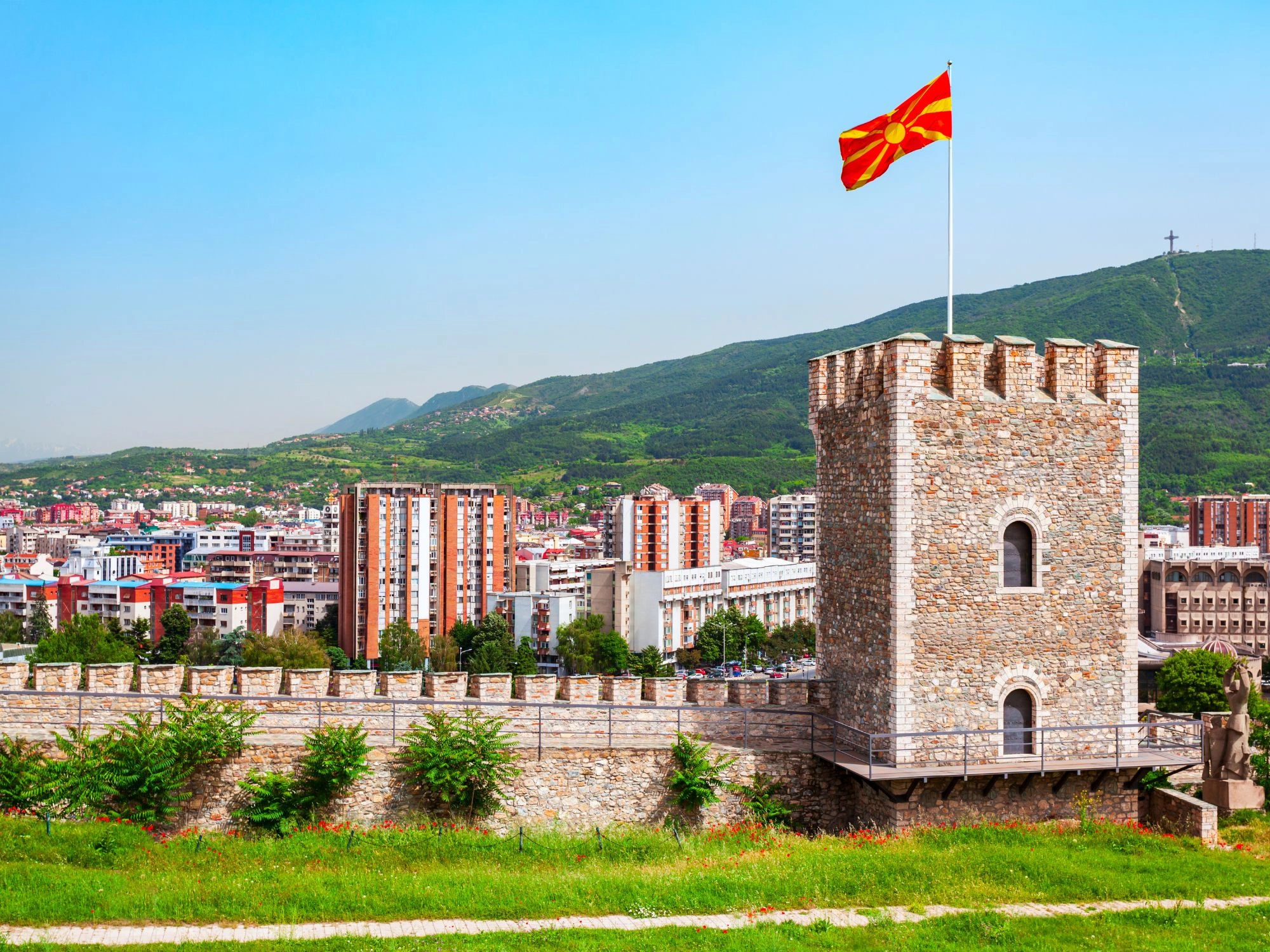 Kale Fortress tower flying the North Macedonian flag, overlooking downtown Skopje and green hills.