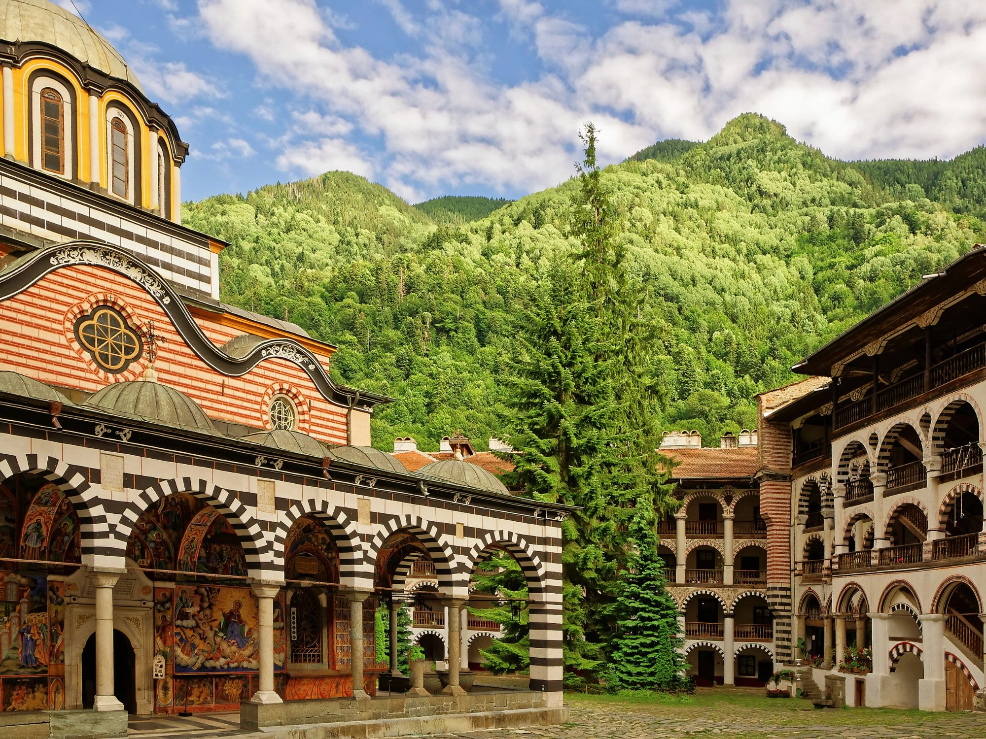 Rila Monastery – striped arches and frescoes surrounded by forested mountains in Bulgaria.