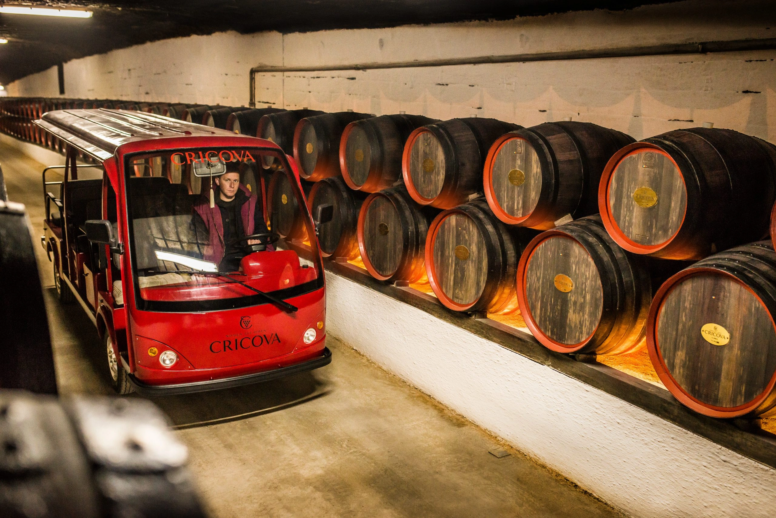 Cricova wine cellars tour cart passing barrels in underground wine tunnel, Moldova.