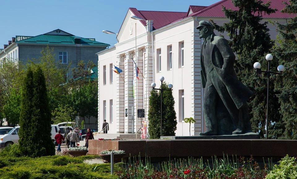 Lenin statue in Comrat, Moldova, near administrative building with flags and red roof.