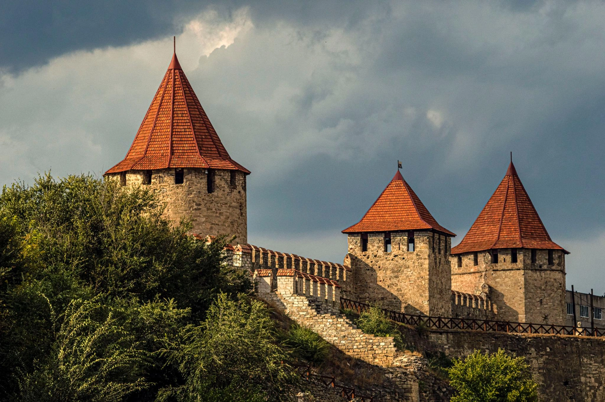 Tighina Fortress towers in Moldova with red-tiled roofs rising above green trees under cloudy skies.