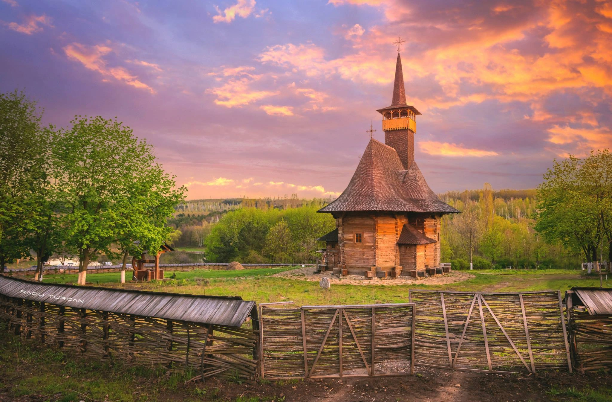 Traditional wooden church in Moldova at sunset with vibrant sky and rustic fencing