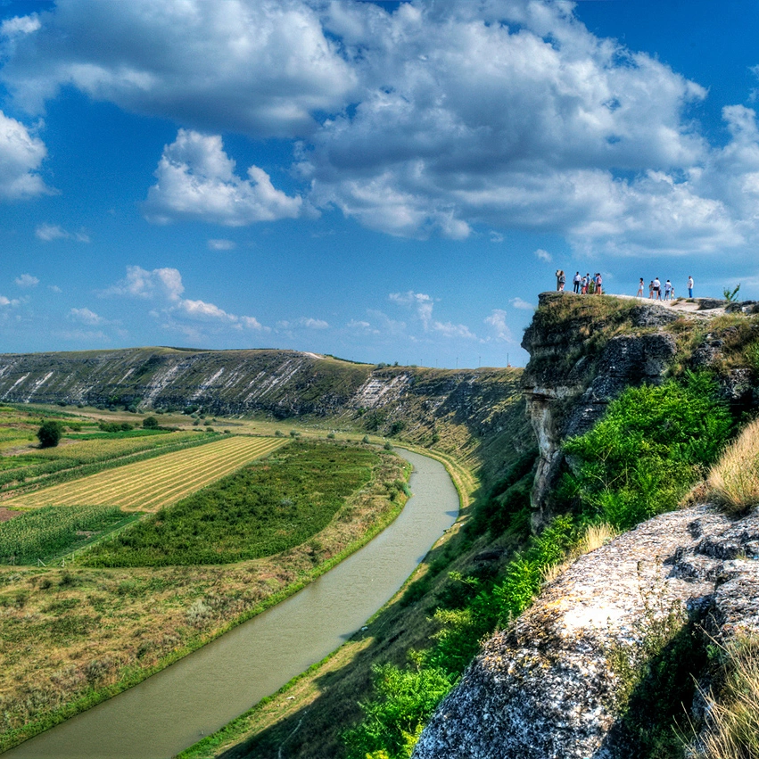 Tourists standing on scenic cliffside viewpoint of Orheiul Vechi in Moldova with winding river below.