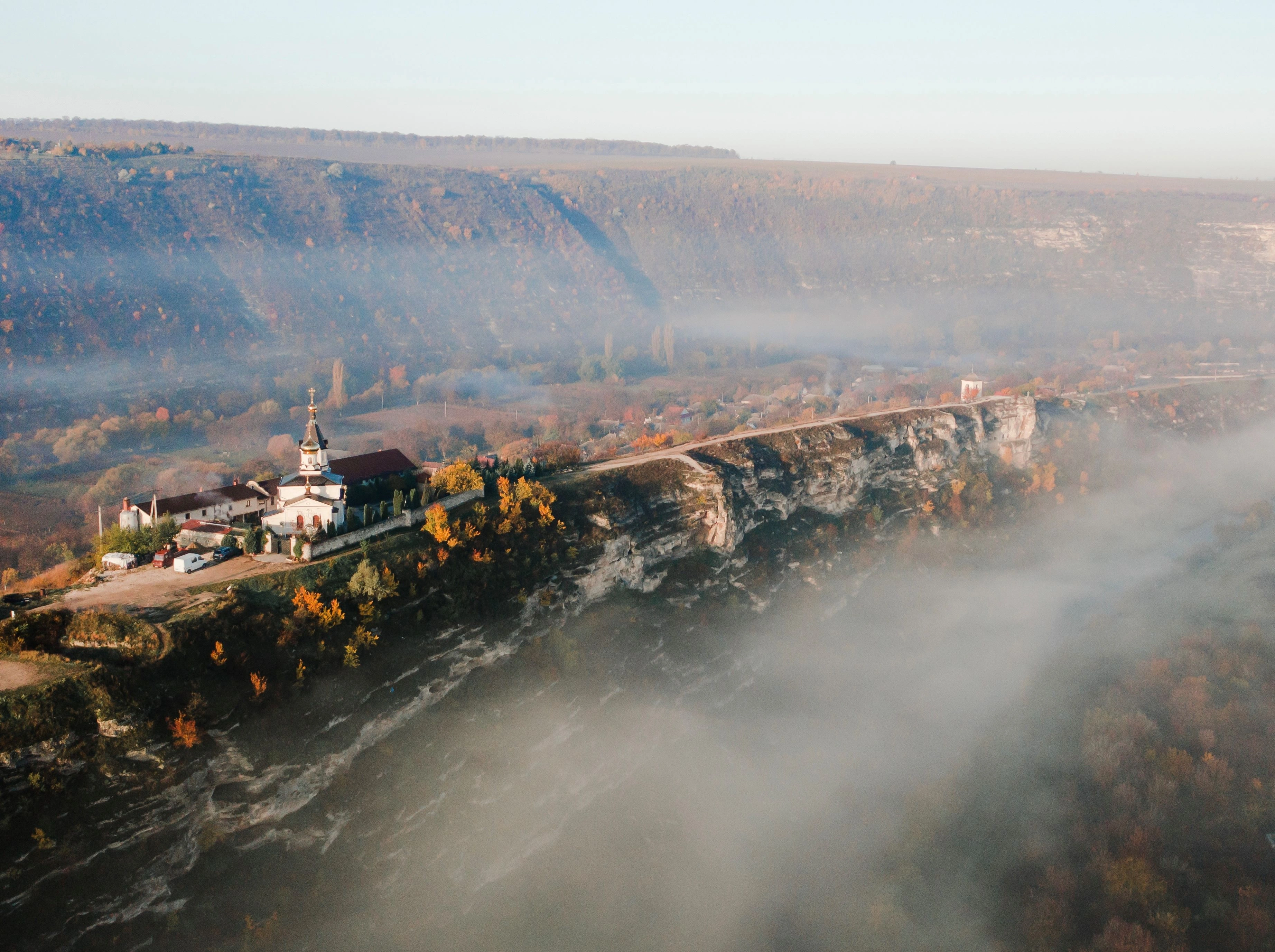 Foggy aerial view of Orheiul Vechi monastery on a cliffside in Moldova's Raut River Valley.