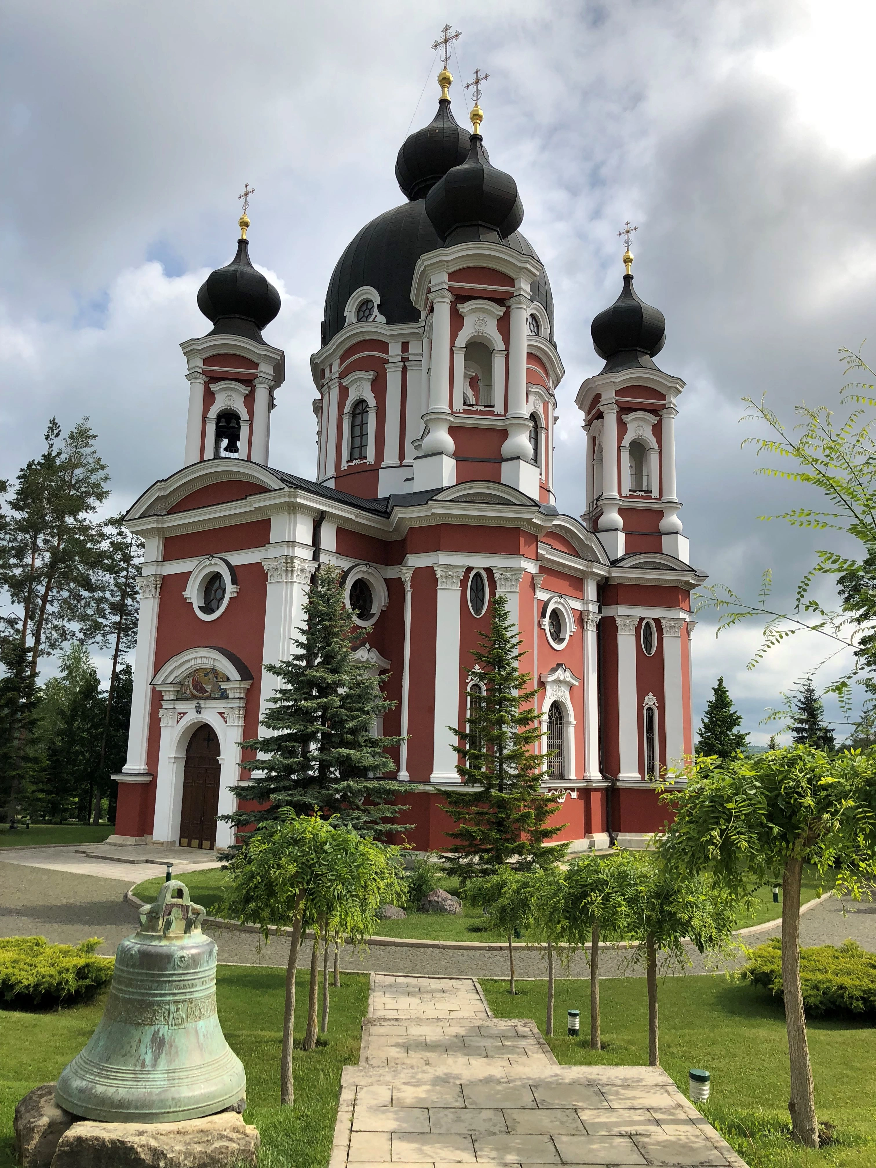 Curchi Monastery in Moldova with red walls and black domes surrounded by greenery.
