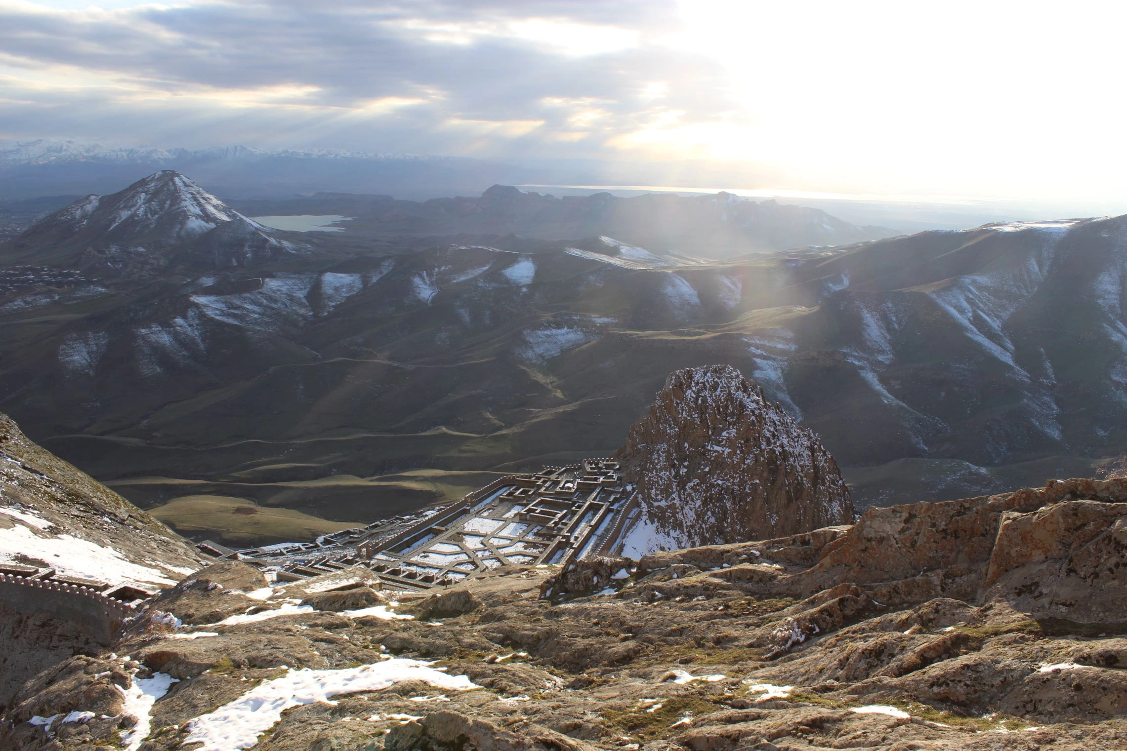 Mountain view of Alinja Castle ruins with snowy peaks and dramatic sunlight in Nakhchivan.