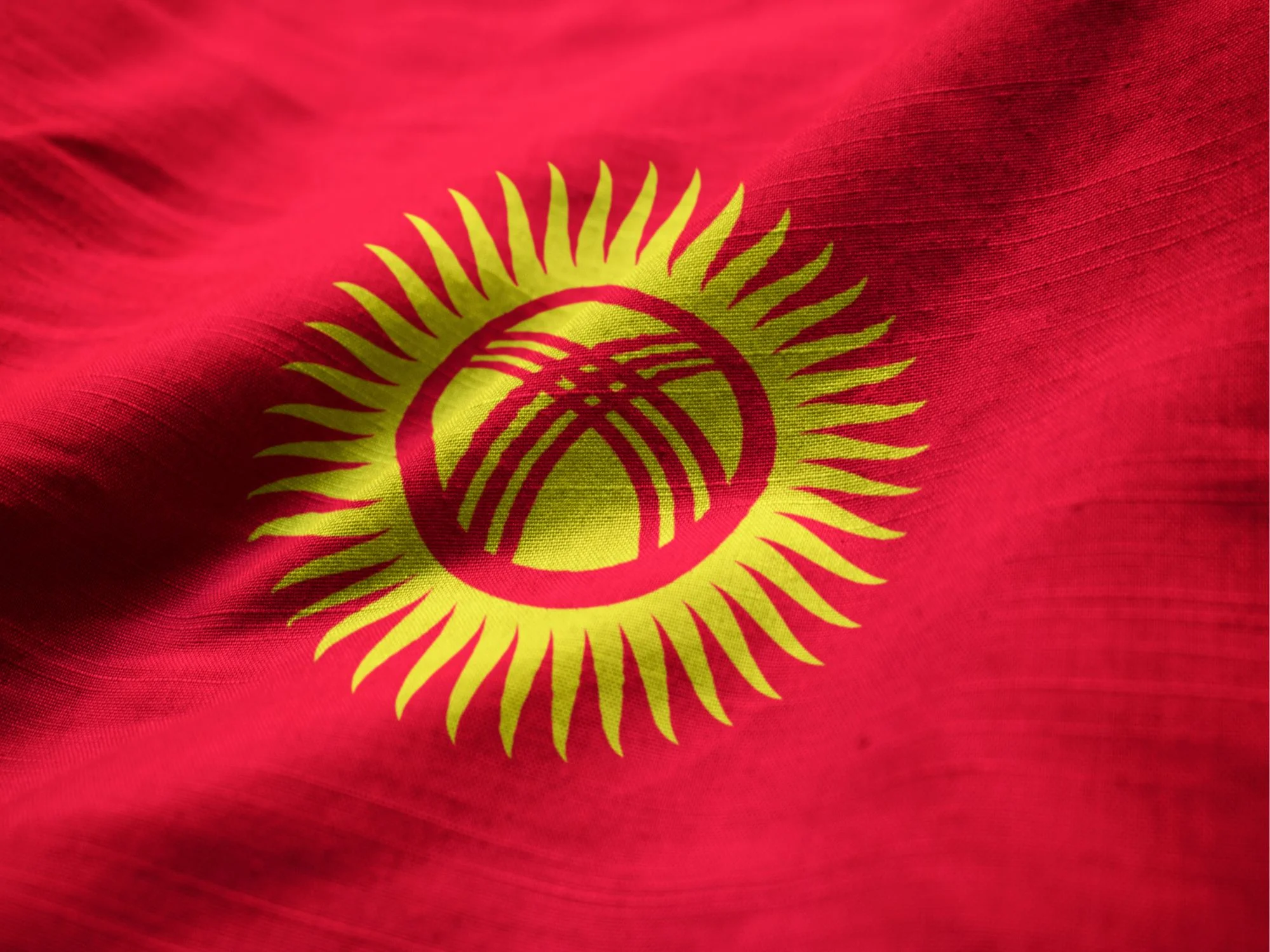 Red flag of Kyrgyzstan with yellow sun and tunduk symbol in the center.