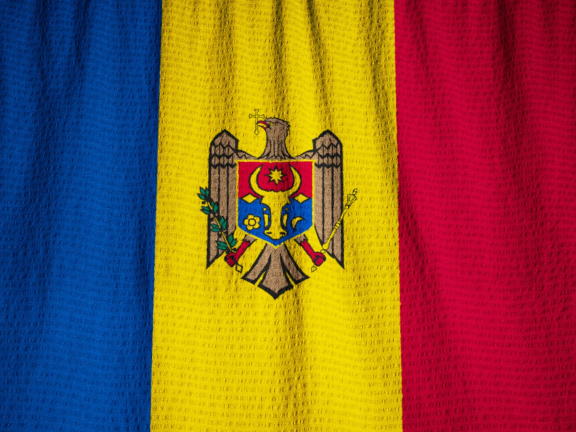 Close-up of Moldova flag with vertical stripes and the national coat of arms centered on yellow.