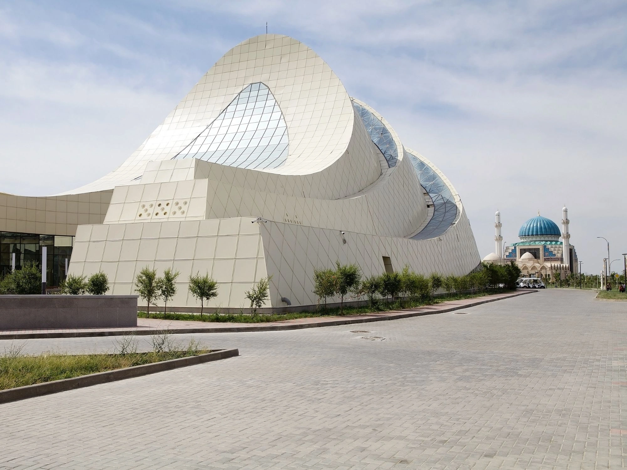 Modern white architectural building in Turkistan with mosque visible in background.