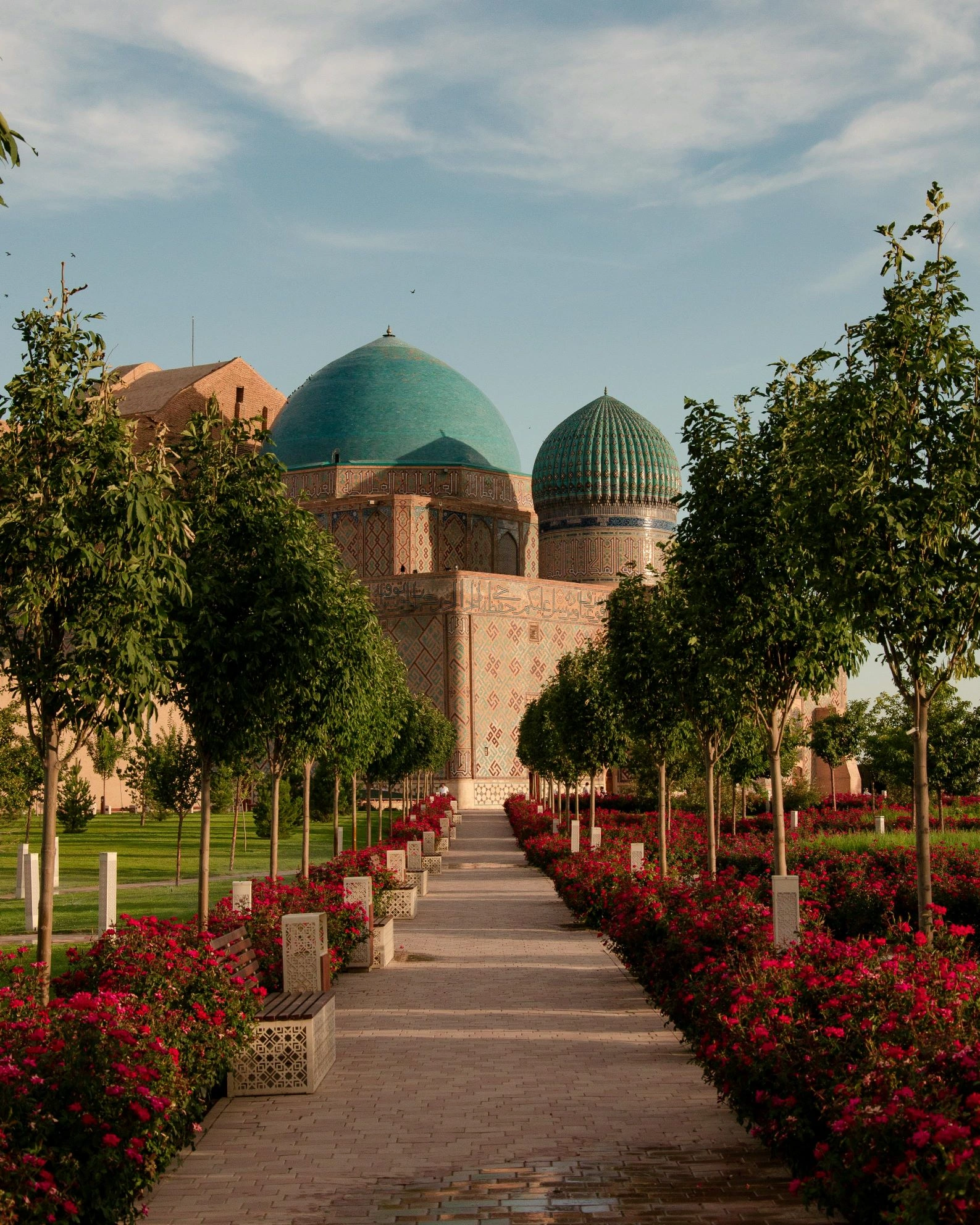 Garden walkway leading to Yasawi Mausoleum with twin turquoise domes in Turkestan, Kazakhstan.