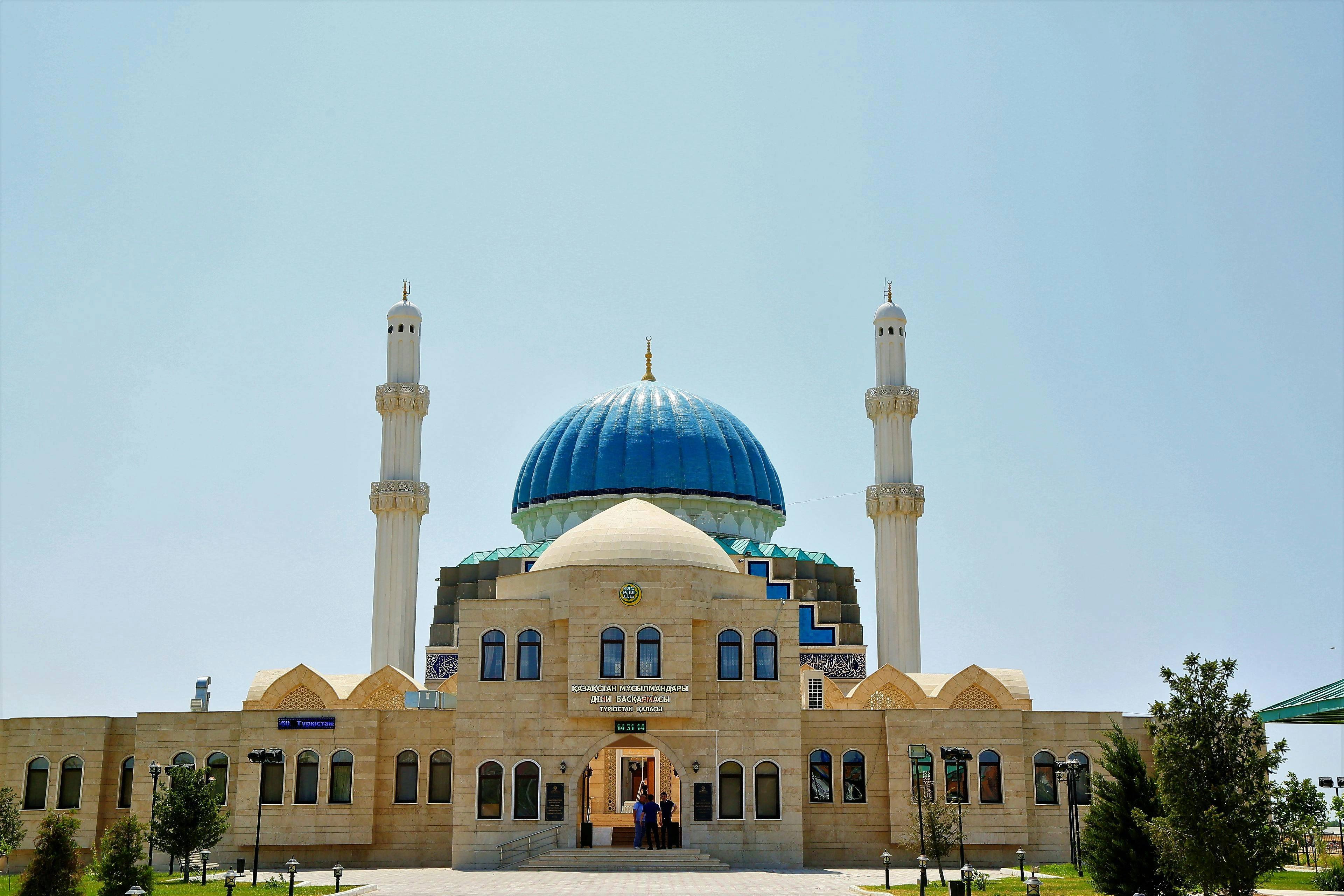 Modern mosque with blue dome and twin minarets under clear blue sky in Kazakhstan.
