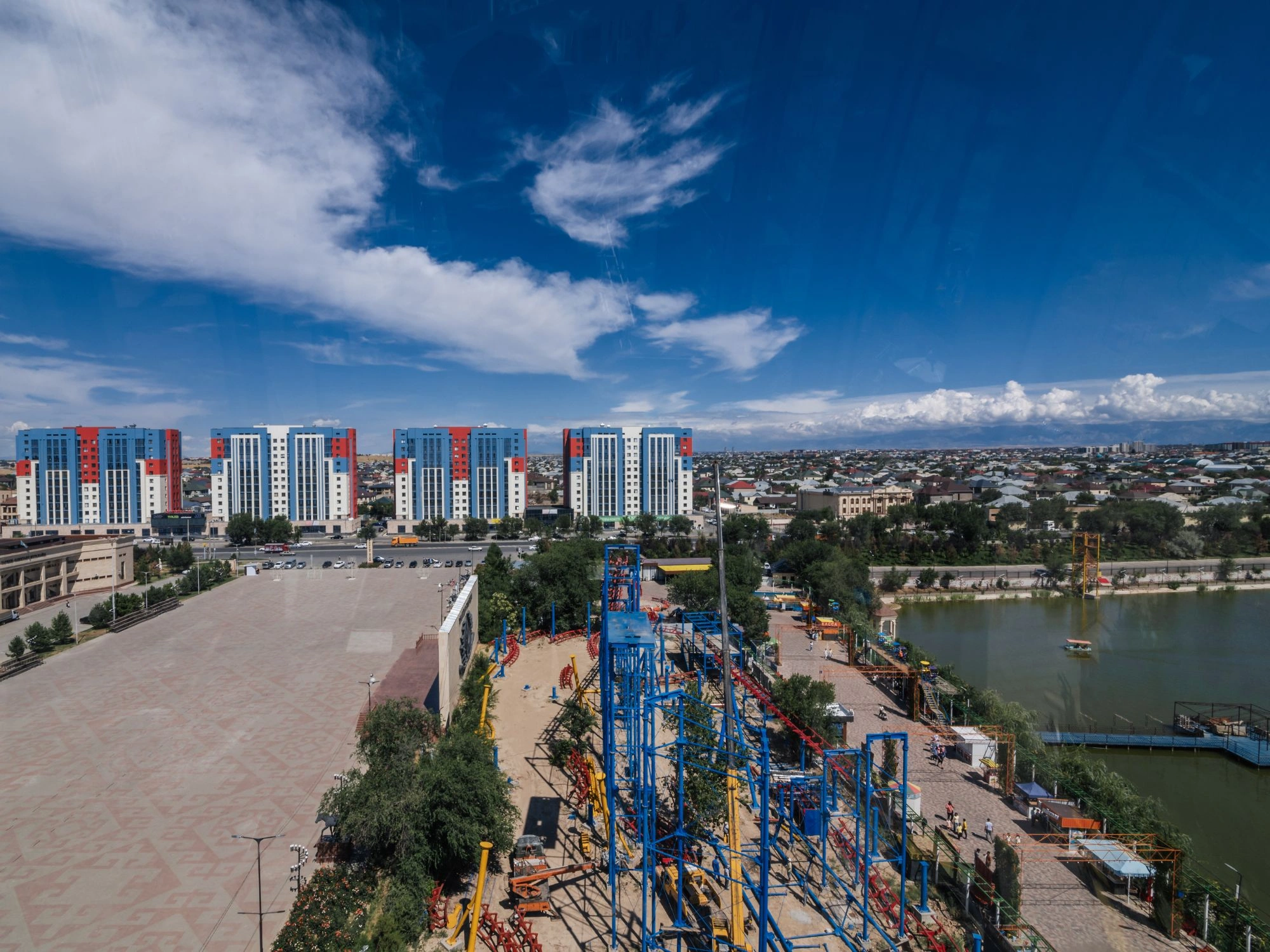 Cityscape of Shymkent with colorful high-rise buildings and amusement park near river.