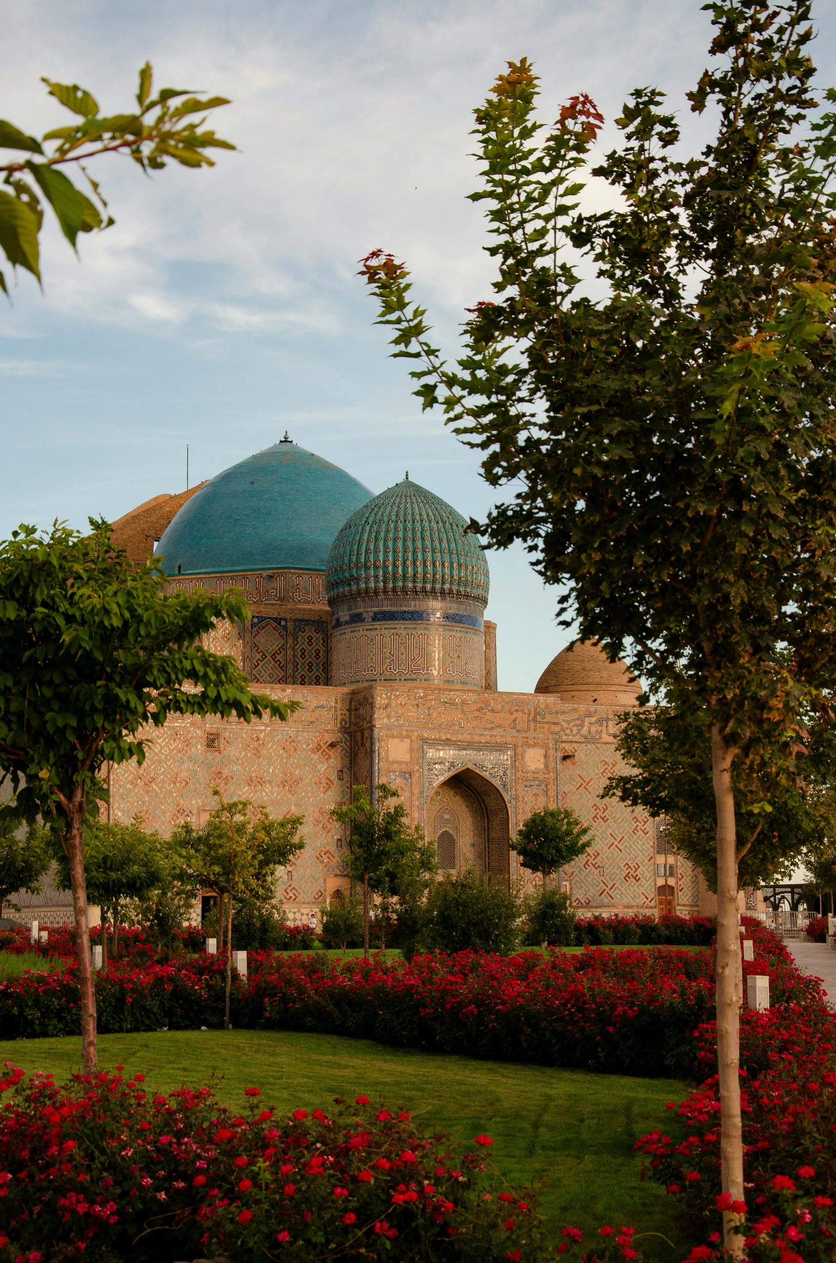 Historic Yasawi Mausoleum framed by trees and red flower beds in southern Kazakhstan.