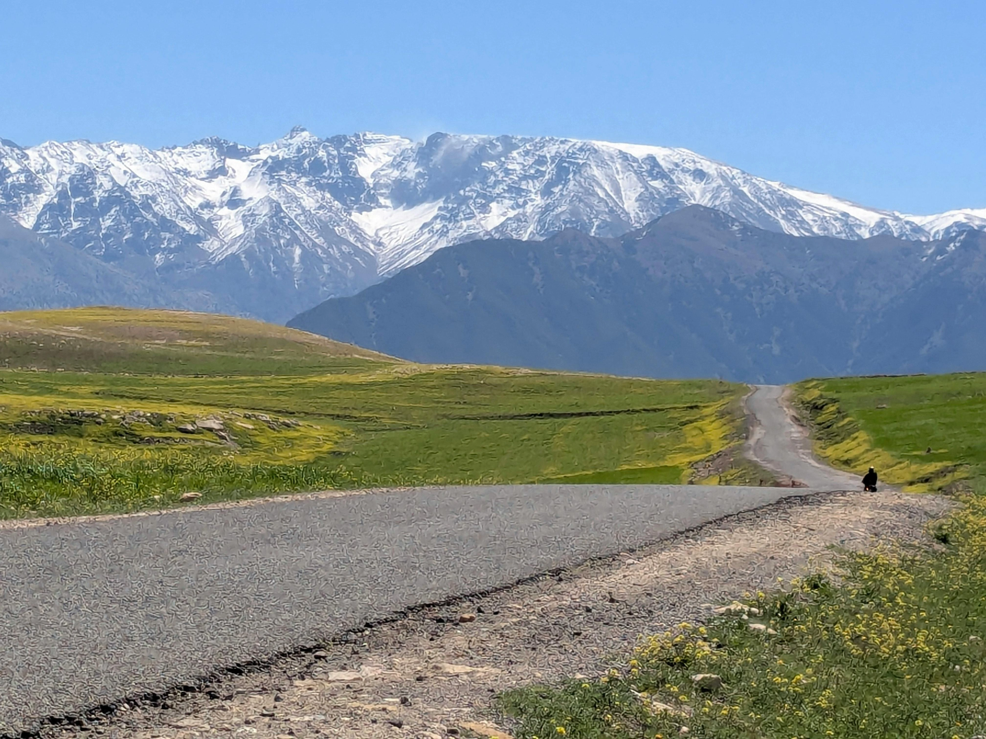 Winding road through Kyrgyz pastureland leading to snow-covered Tien Shan mountains.
