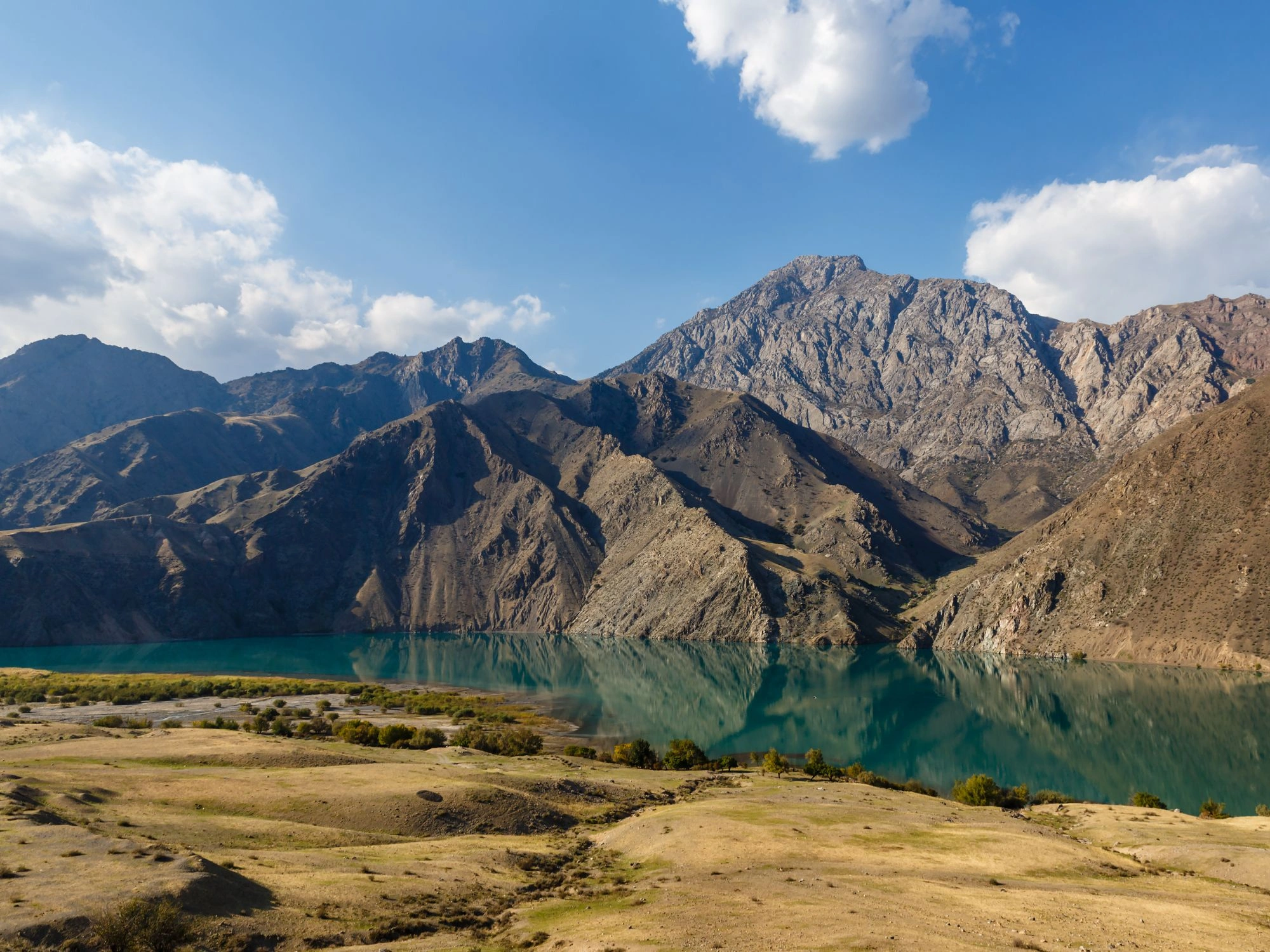 Naryn River flowing through rugged Kyrgyz mountains under a blue sky with scattered clouds.