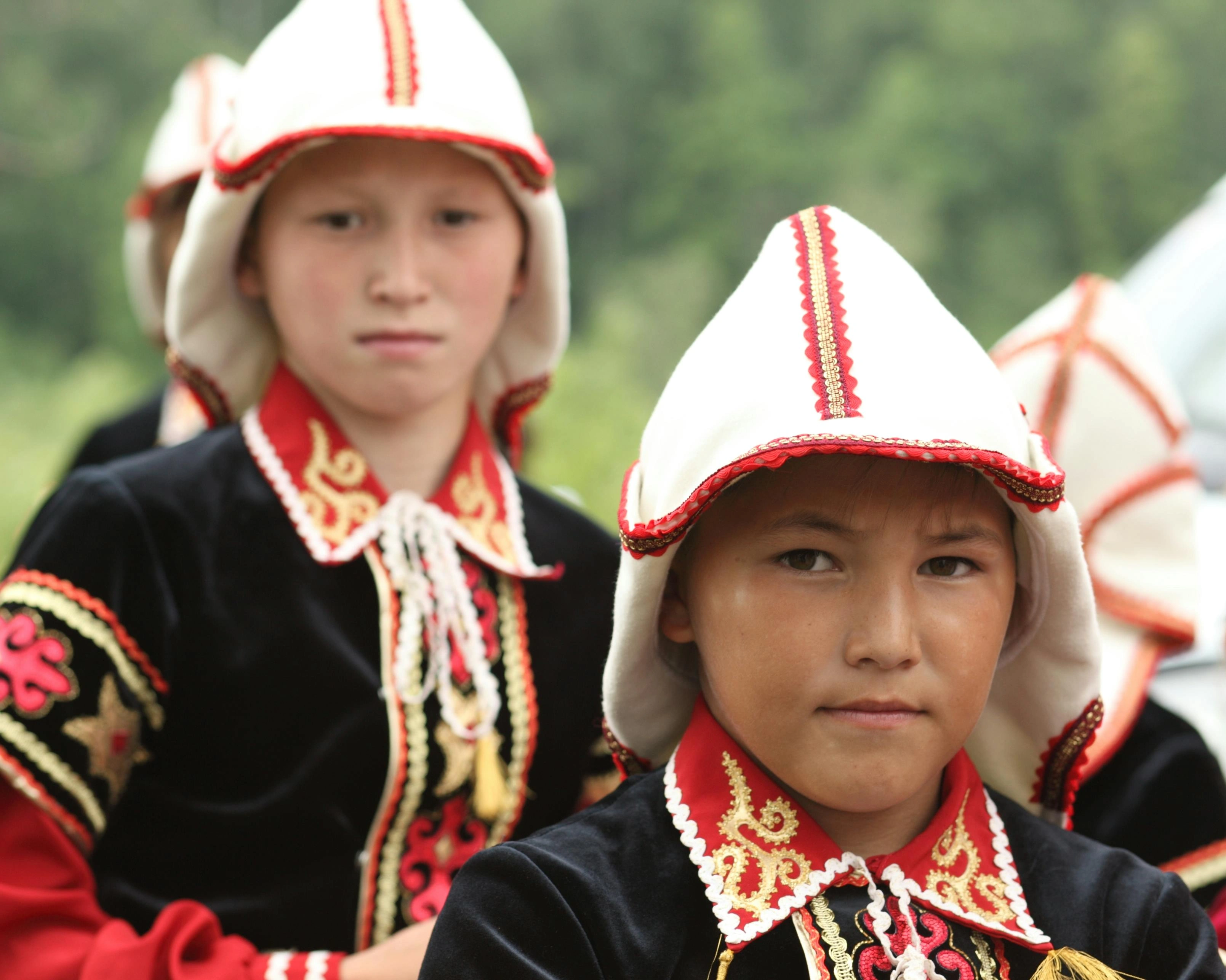 Kyrgyz children in traditional embroidered clothing and kalpak hats during a cultural event.